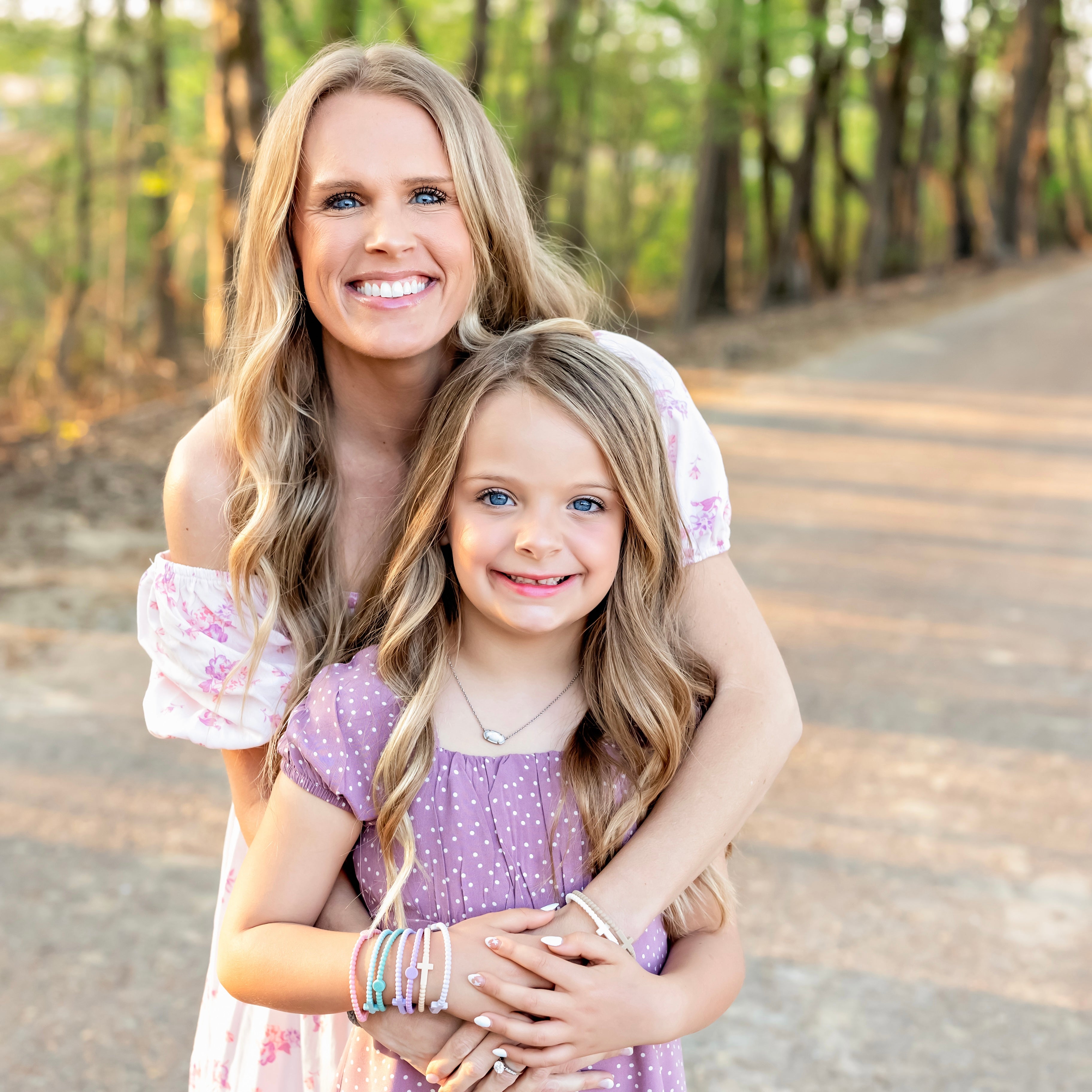Woman and young girl hugging outdoors on a path with trees in the background
