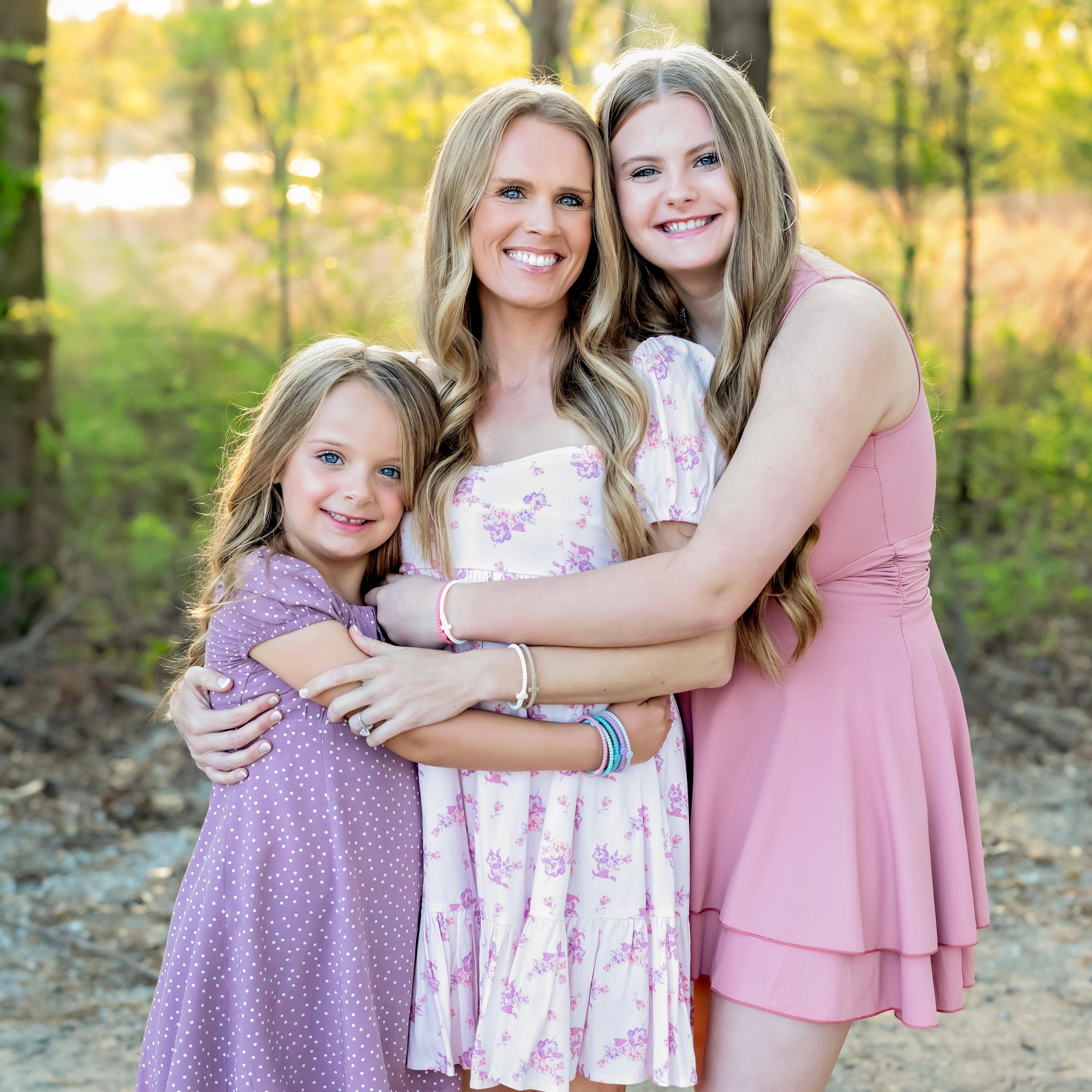 Three women hugging outdoors with a natural background