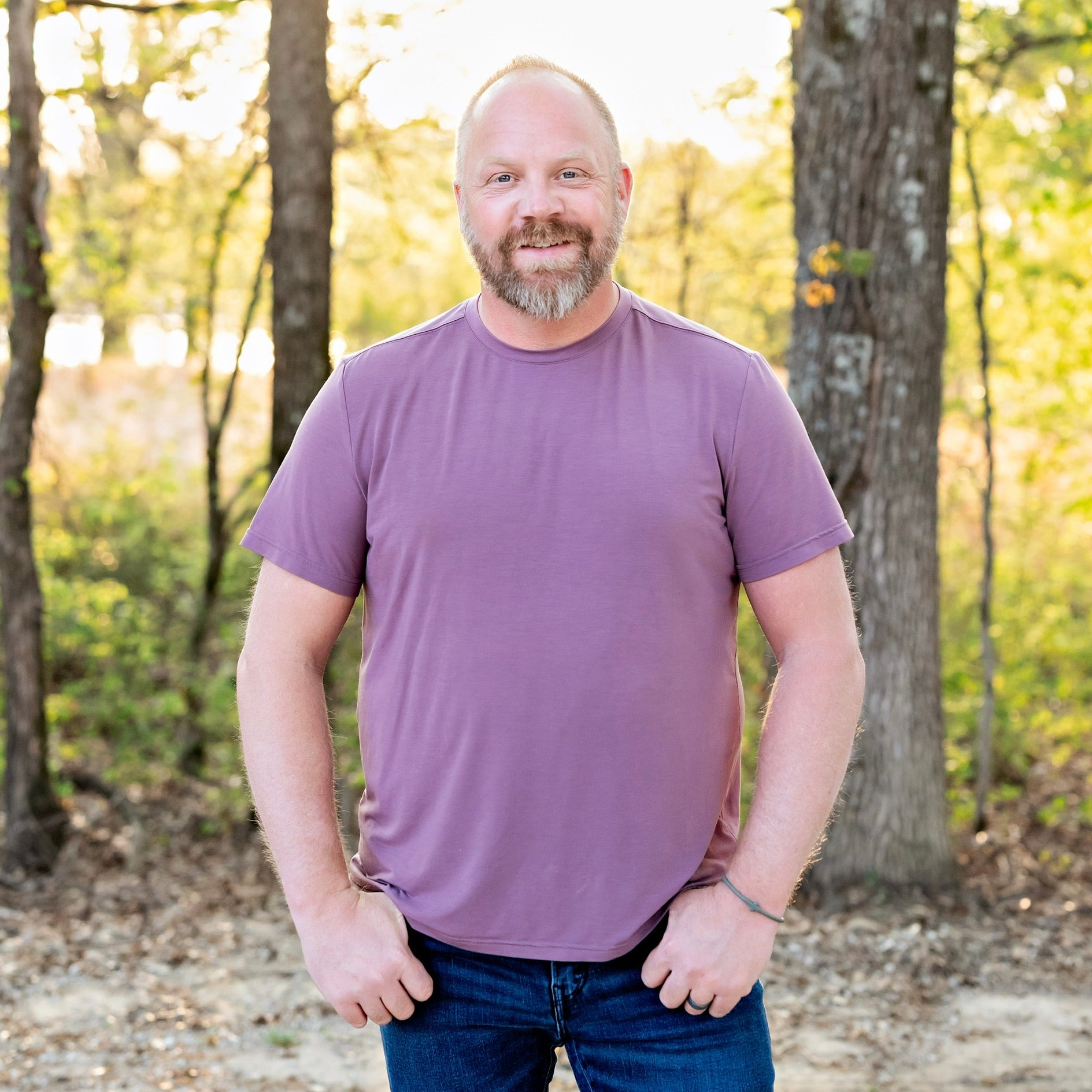 Man wearing a purple shirt standing in a forest