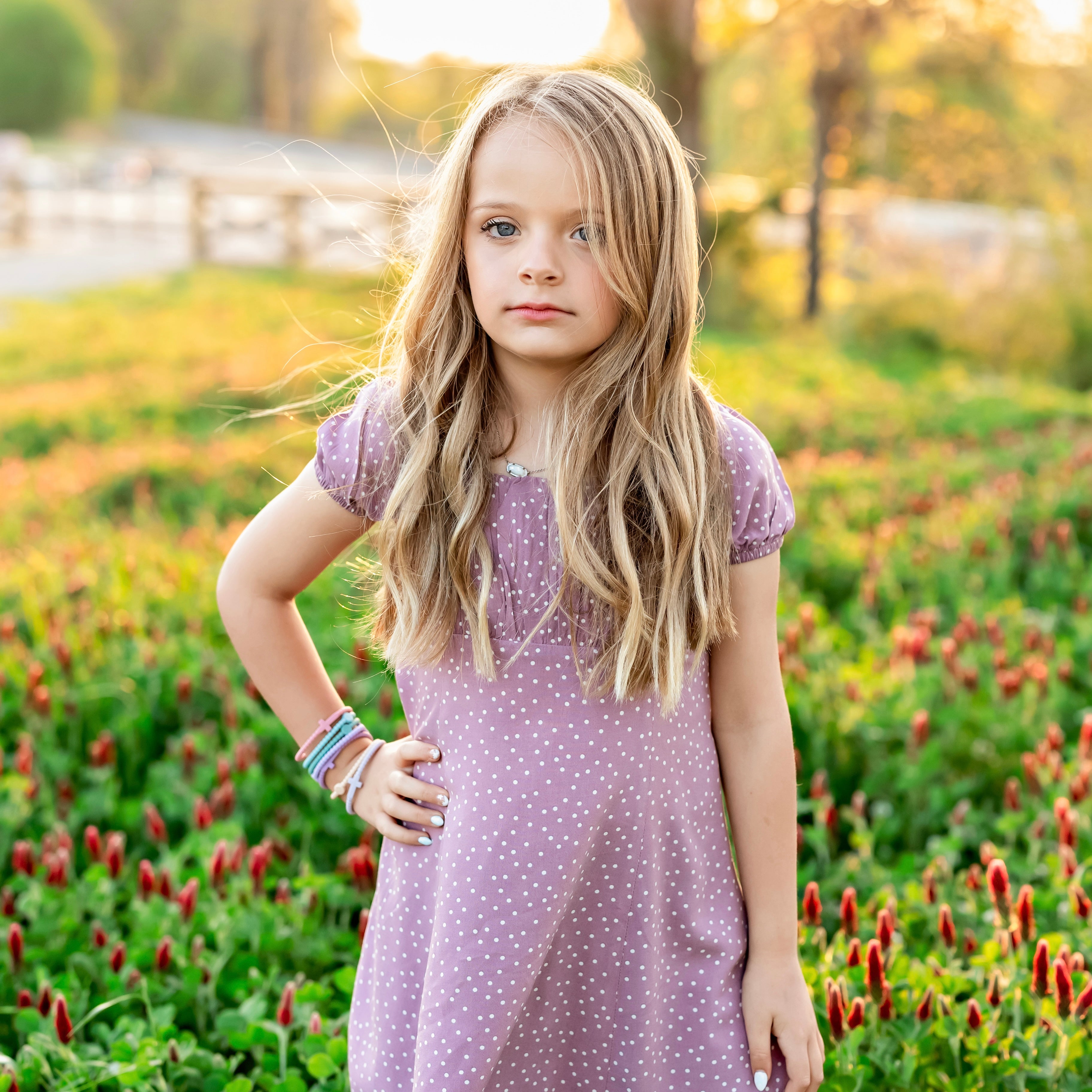 Young girl in a purple polka dot dress standing in a field with flowers.