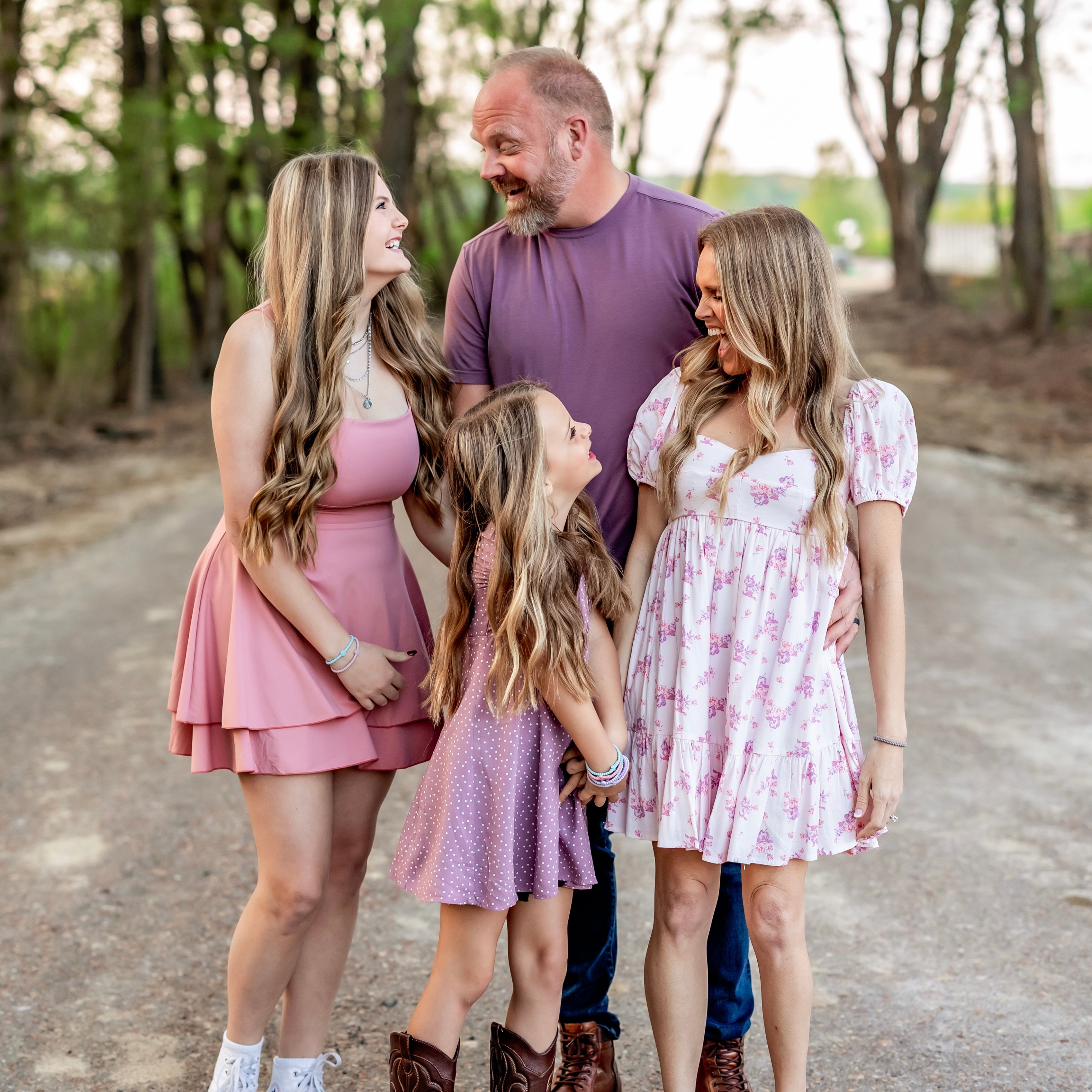 Family of four standing on a dirt road with trees in the background