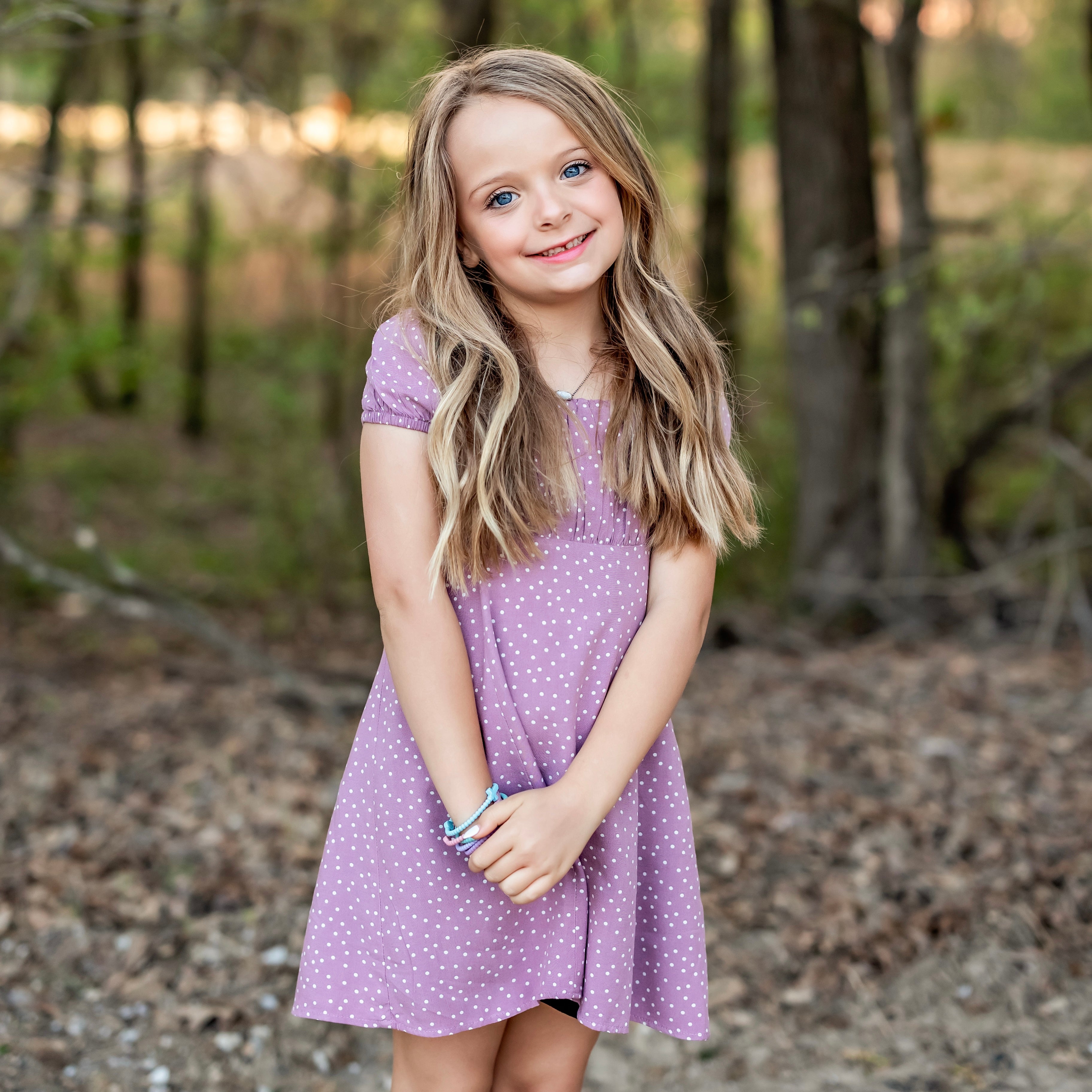 Young girl in a purple polka dot dress standing in a forest setting