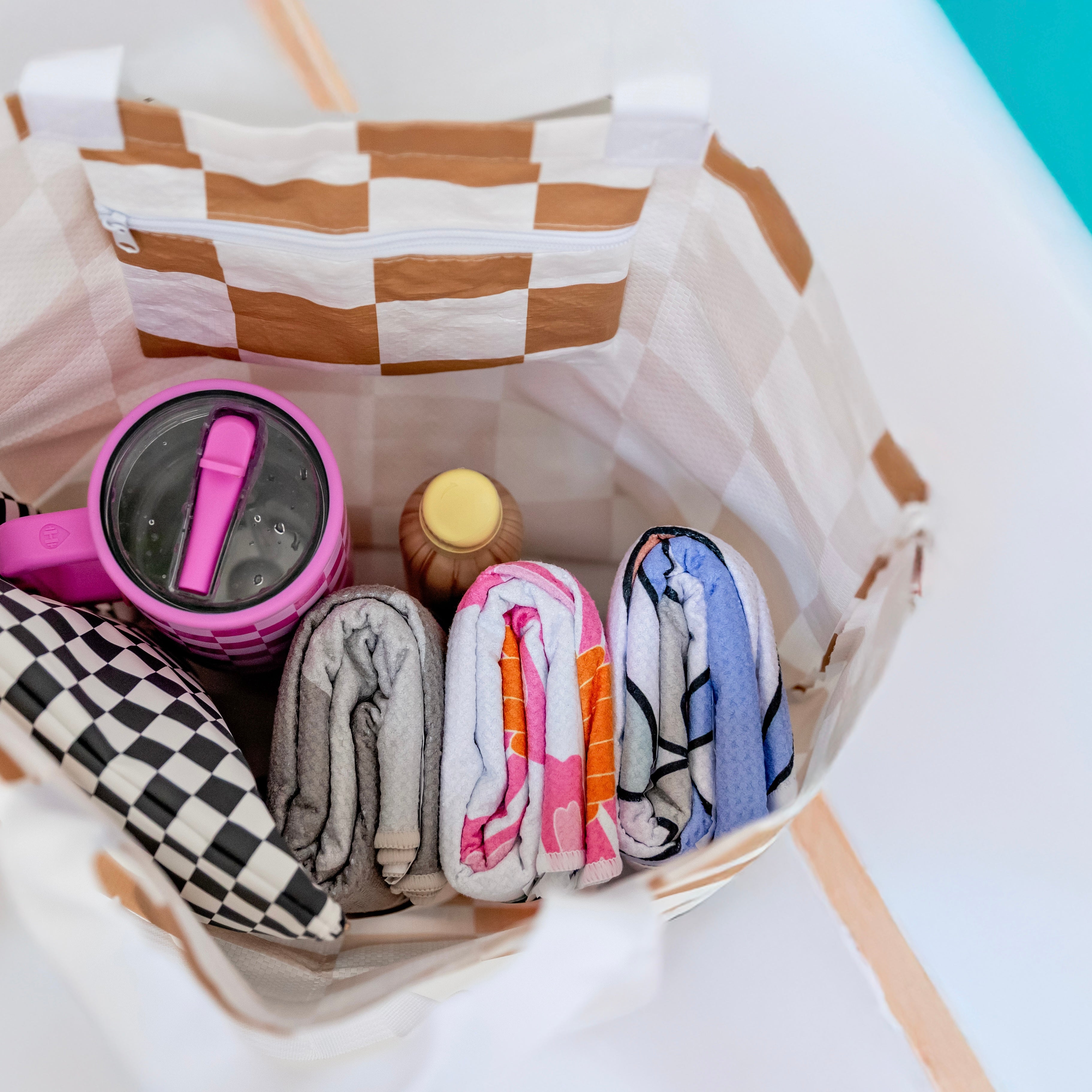Checkered bag with folded clothes and a pink cup on a white surface