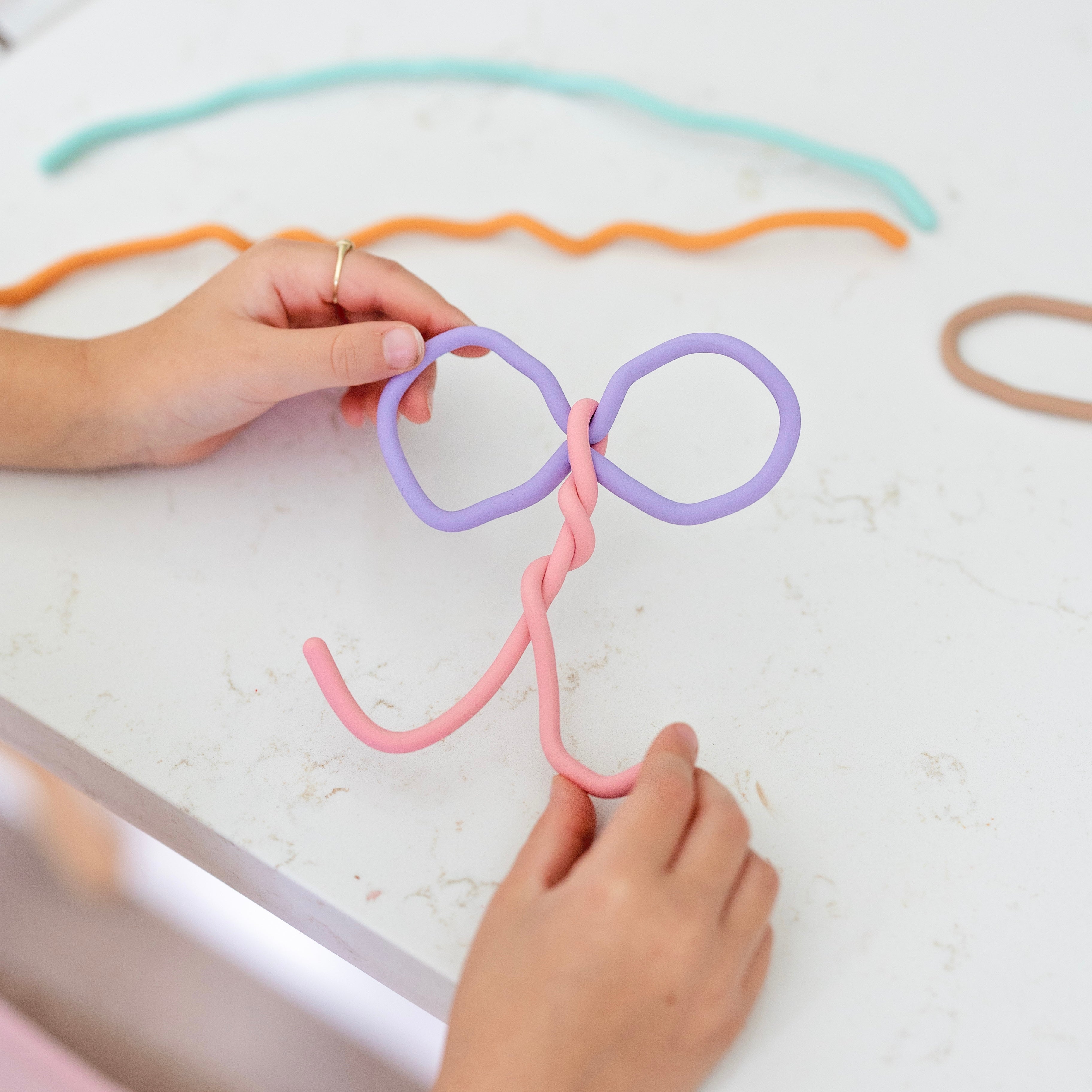 Colorful hair ties being shaped into a bow on a white surface.