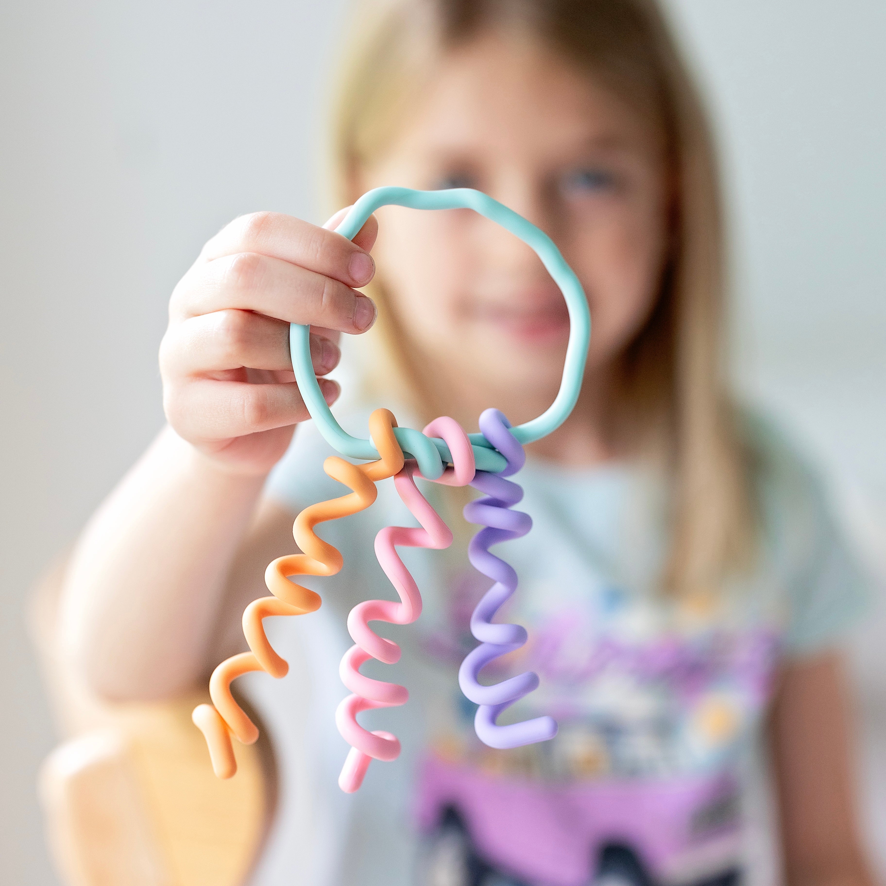 Child holding a colorful spiral teething ring against a neutral background