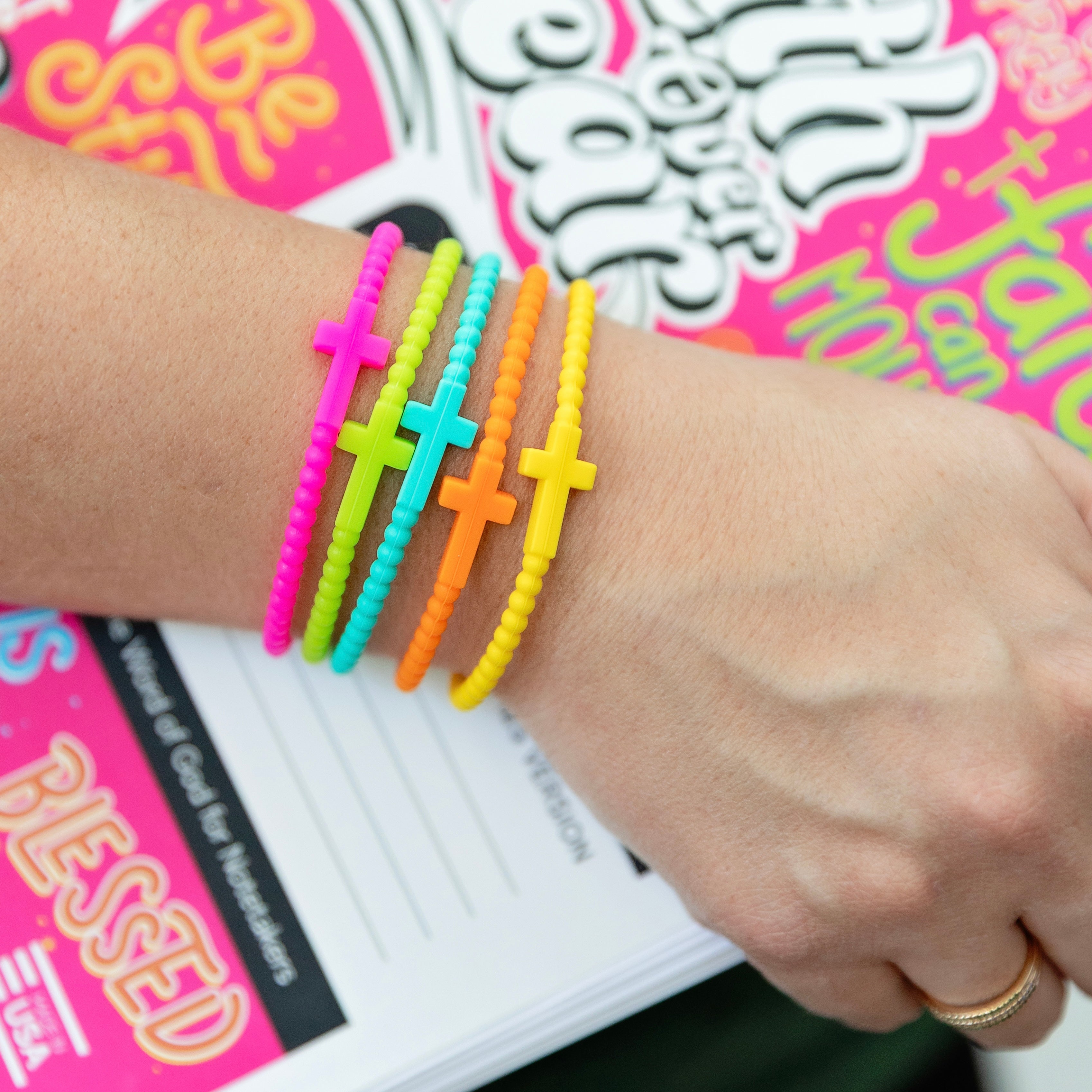 Colorful cross-shaped bracelets on a wrist with a magazine in the background