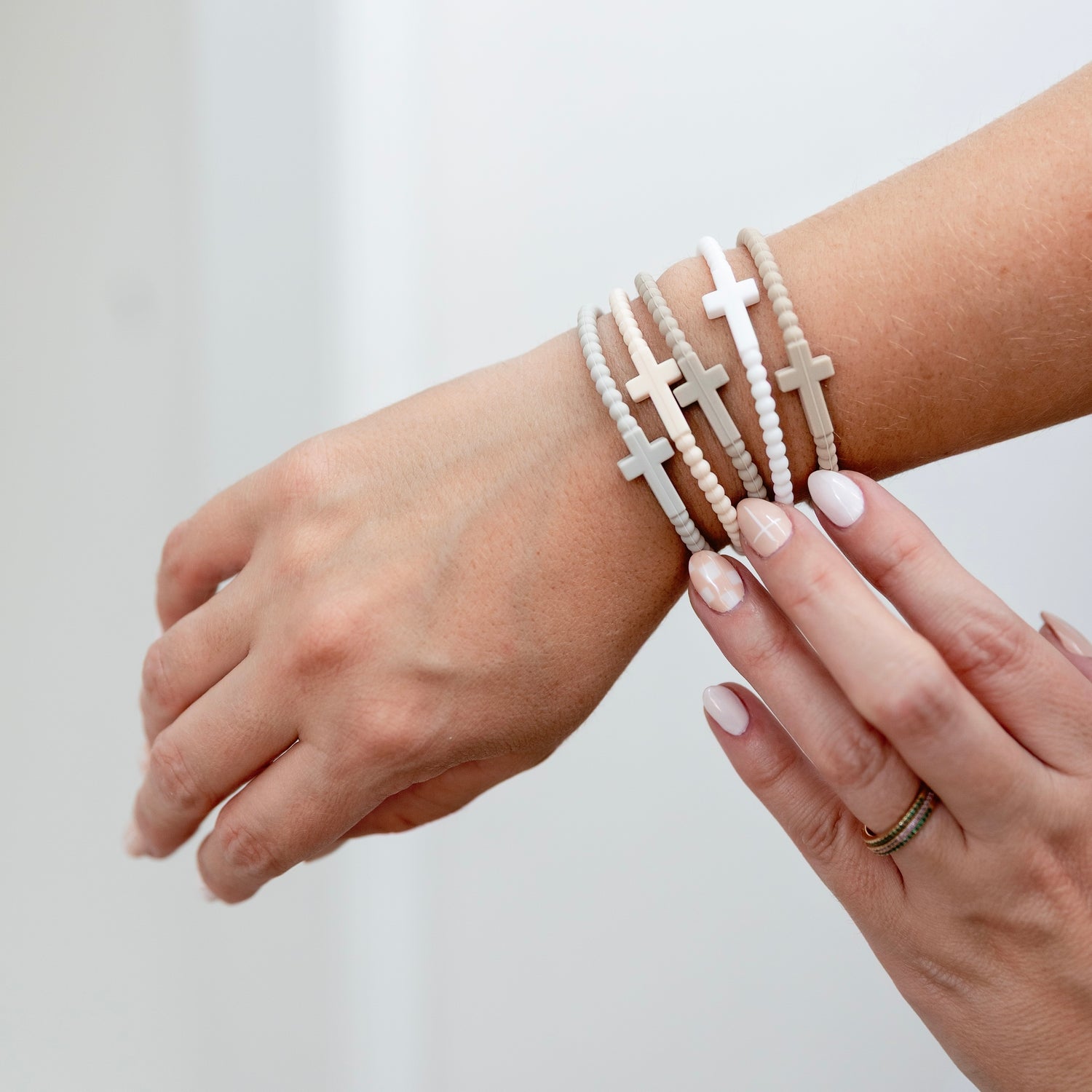 Close-up of a wrist wearing multiple white beaded bracelets with cross designs on a light background.