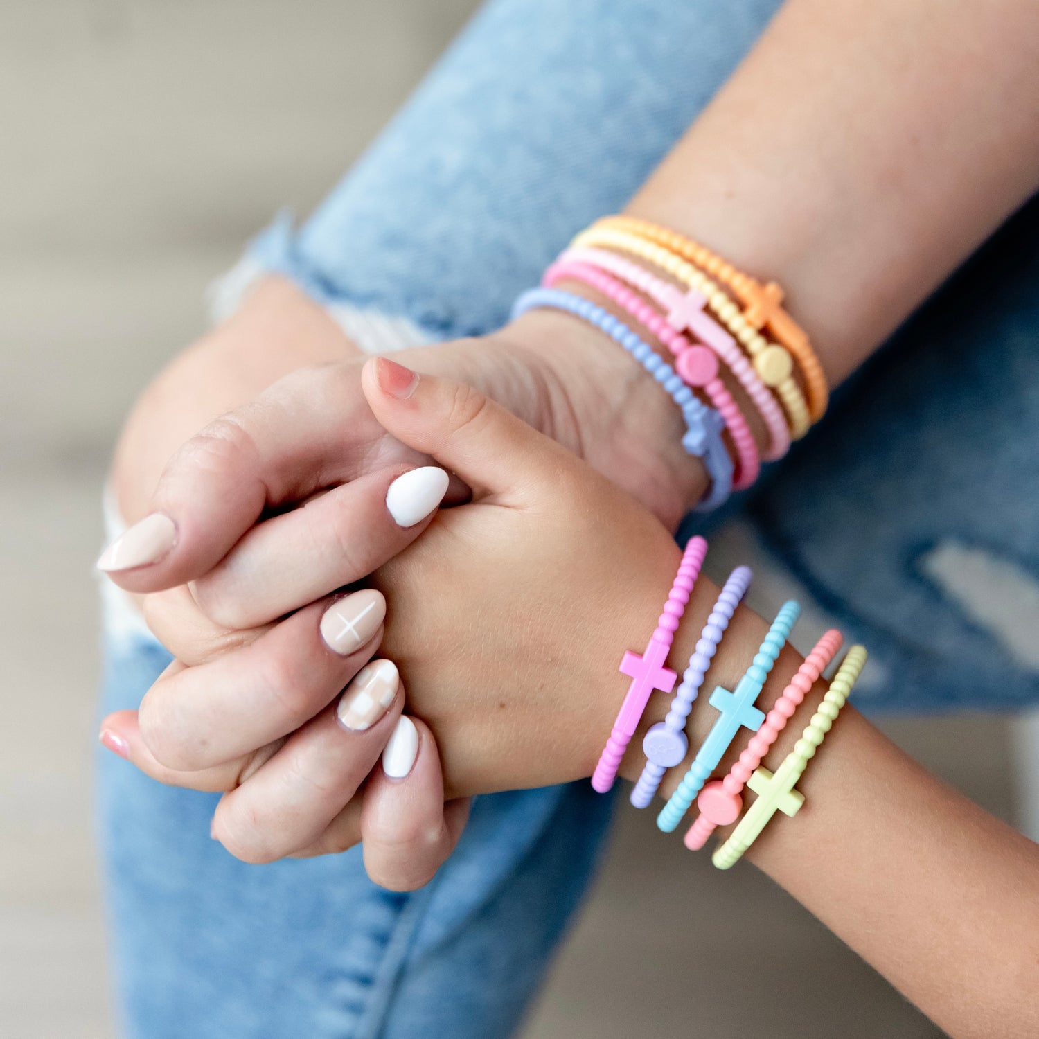Two pairs of hands holding each other, wearing colorful bracelets.