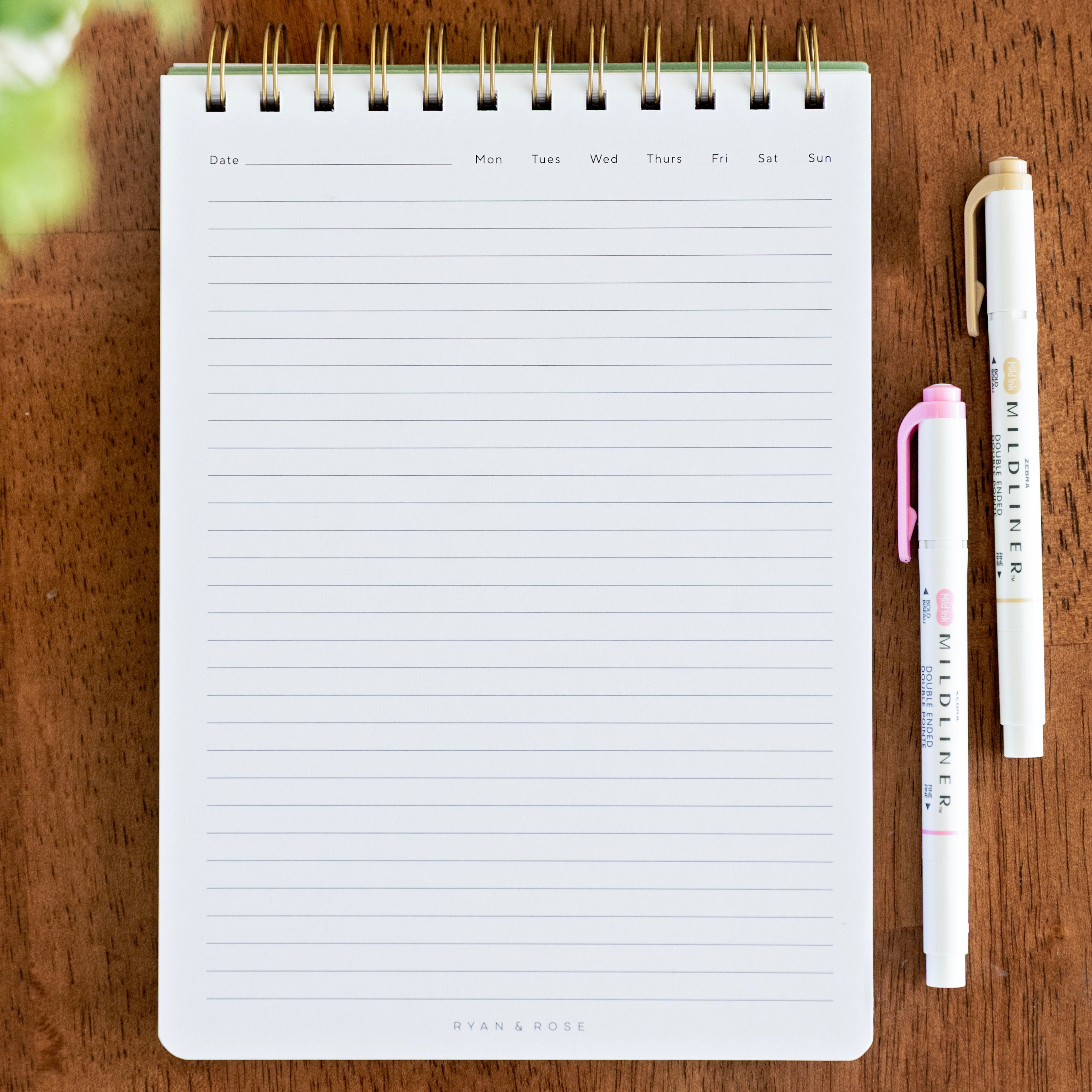 Notebook with lined pages on a wooden surface with two pens.