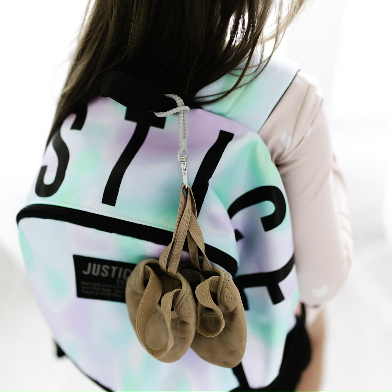 Girl wearing a back pack with a Cutie Loop attached holding her ballet shoes.