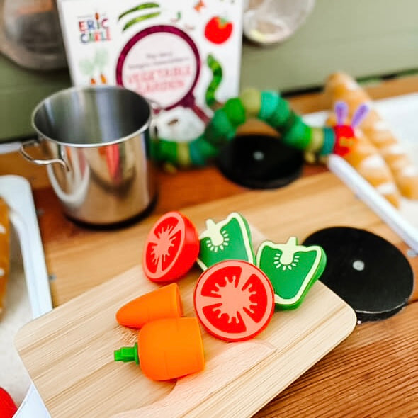 Colorful toy vegetables on a wooden board with a blurred kitchen background