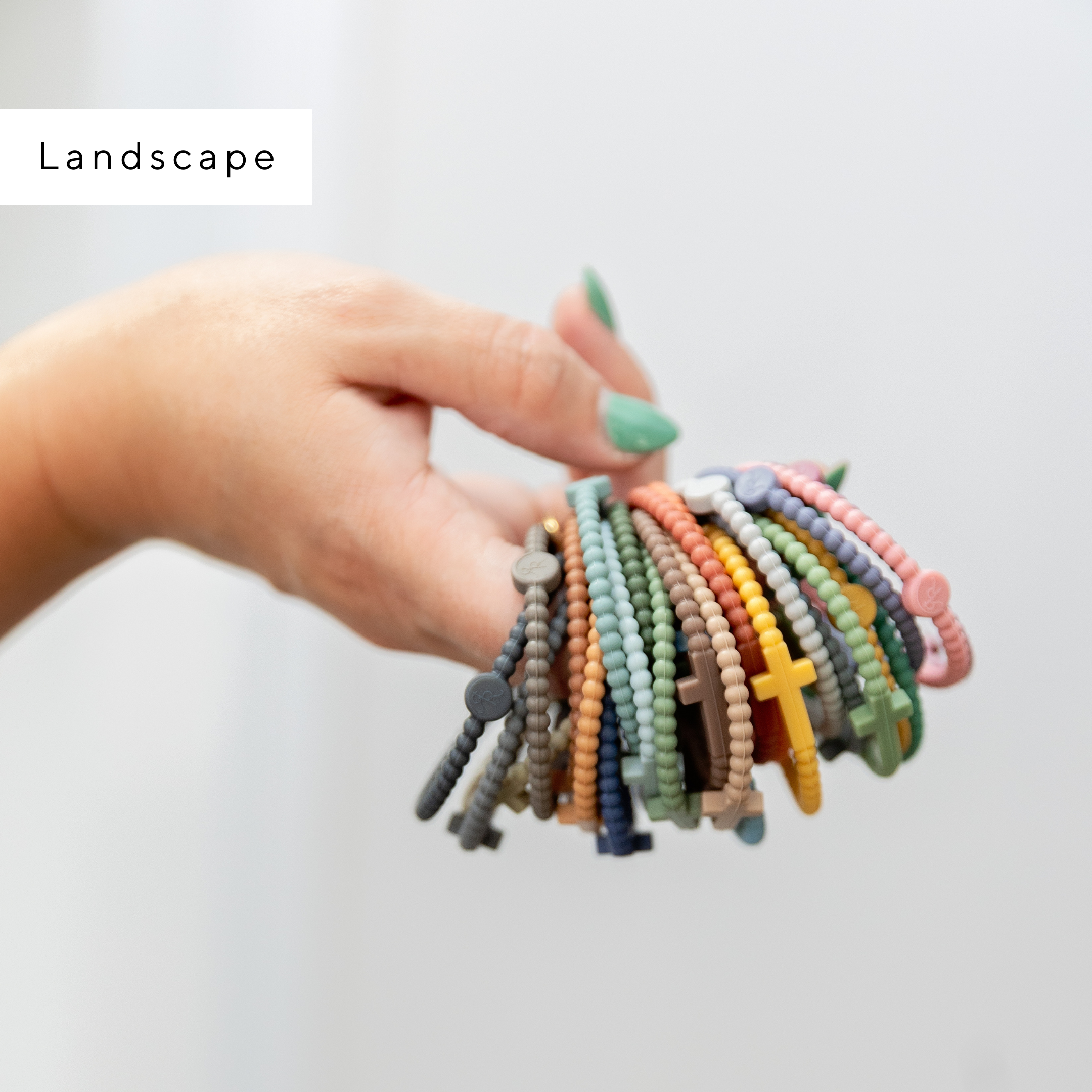 Hand holding a collection of colorful beaded bracelets against a light background