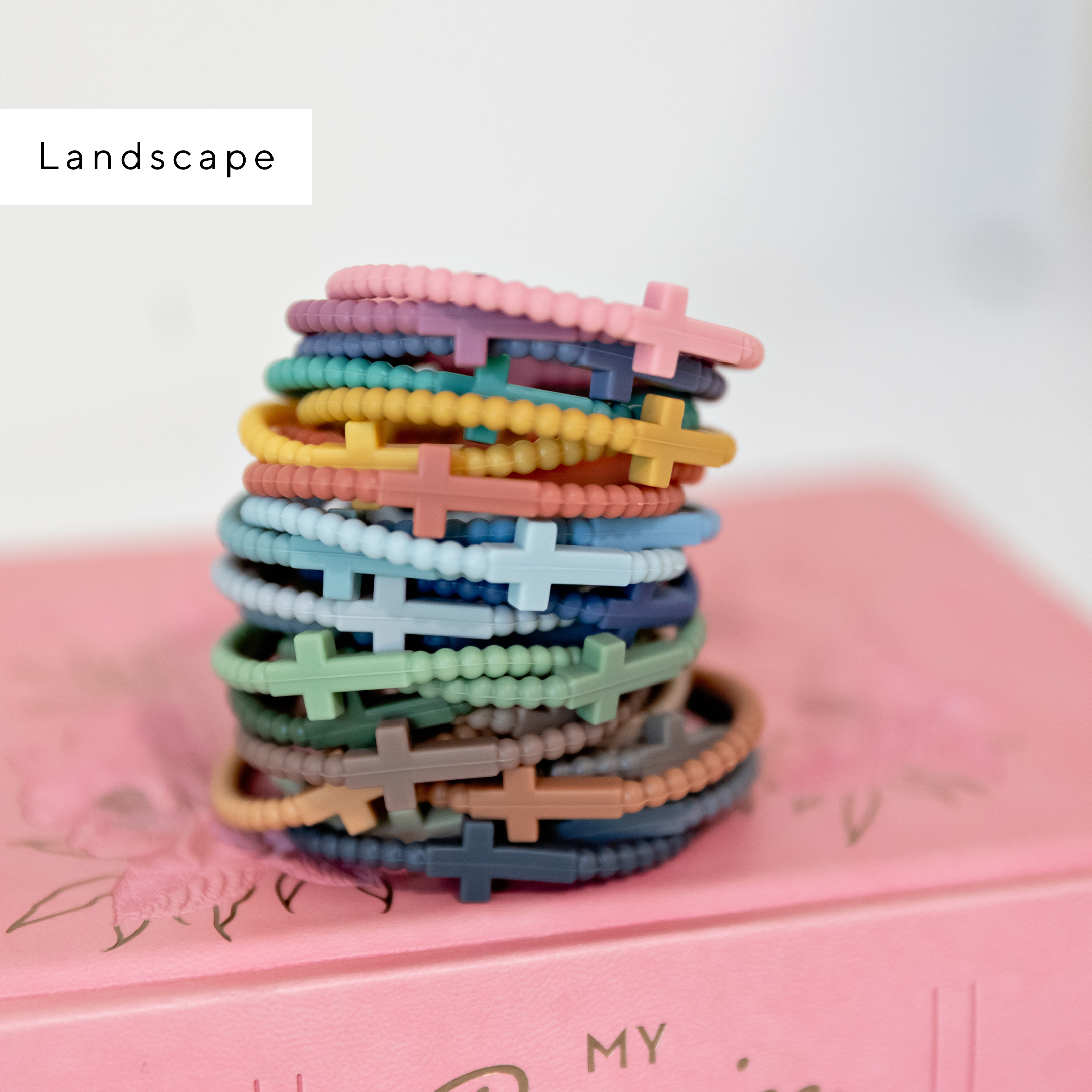 Stack of colorful bracelets on a pink surface with &