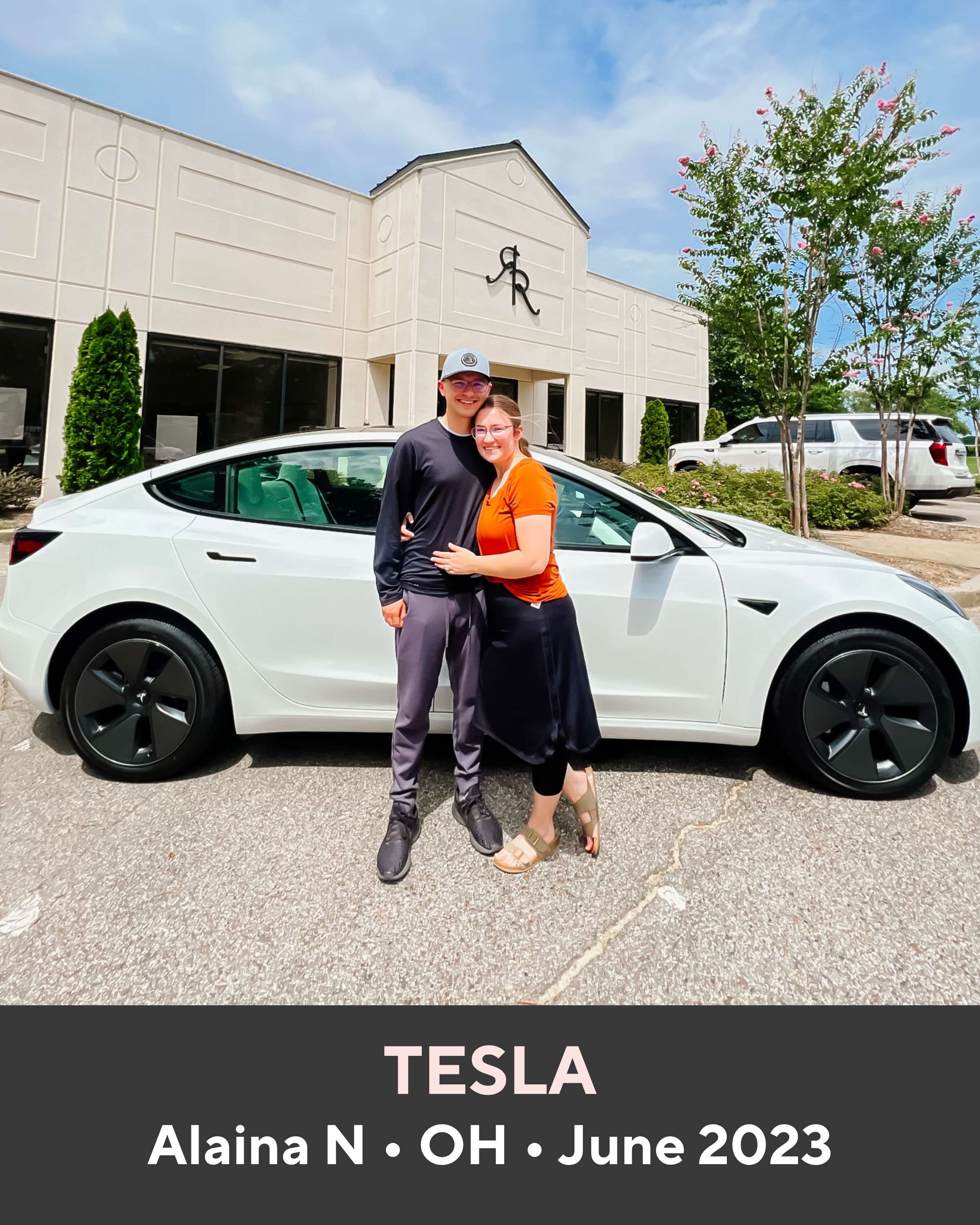 Two people standing next to a white Tesla car in front of a building with a Tesla logo.