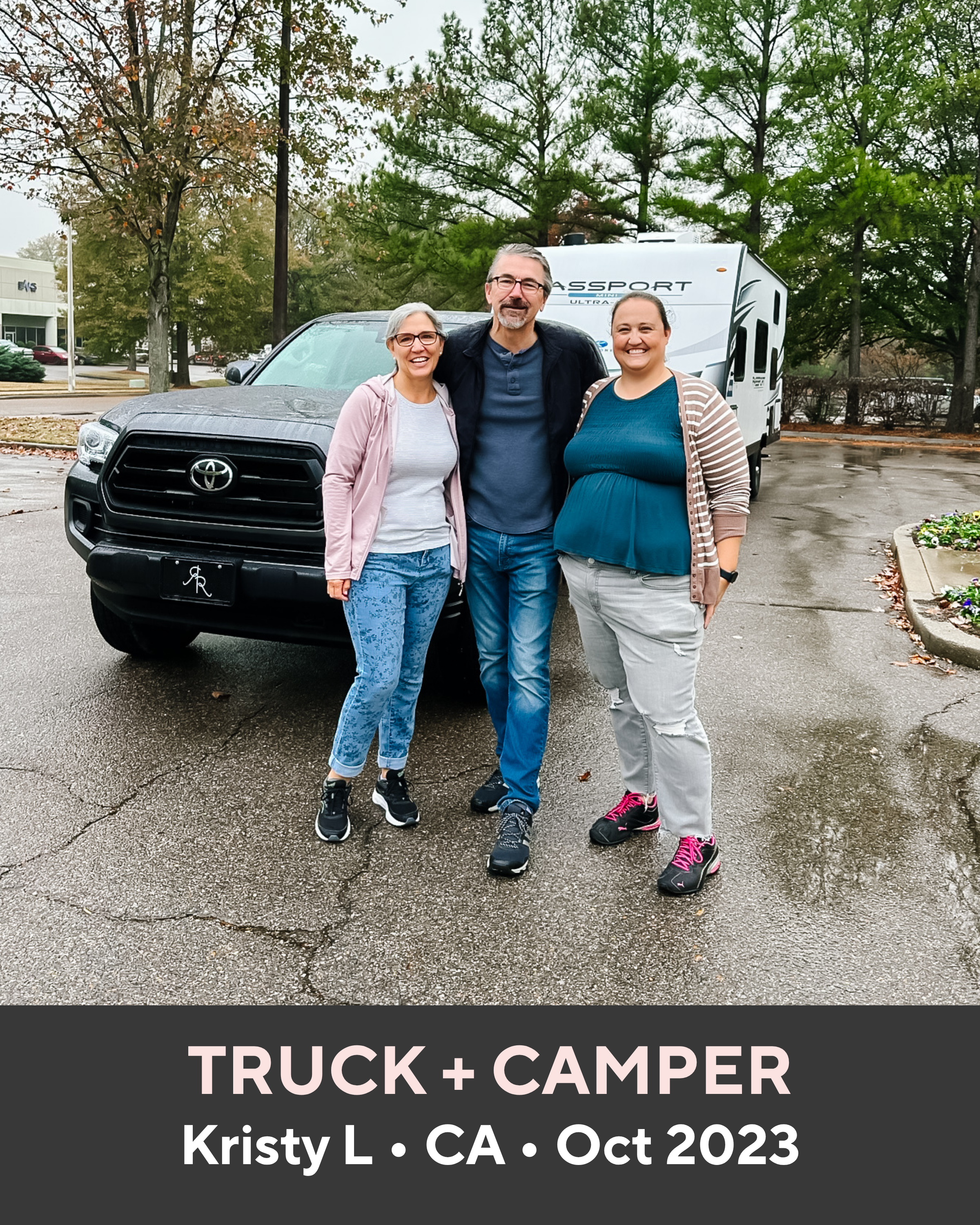 Three people standing in front of a black truck and white camper, with trees and pavement in the background.