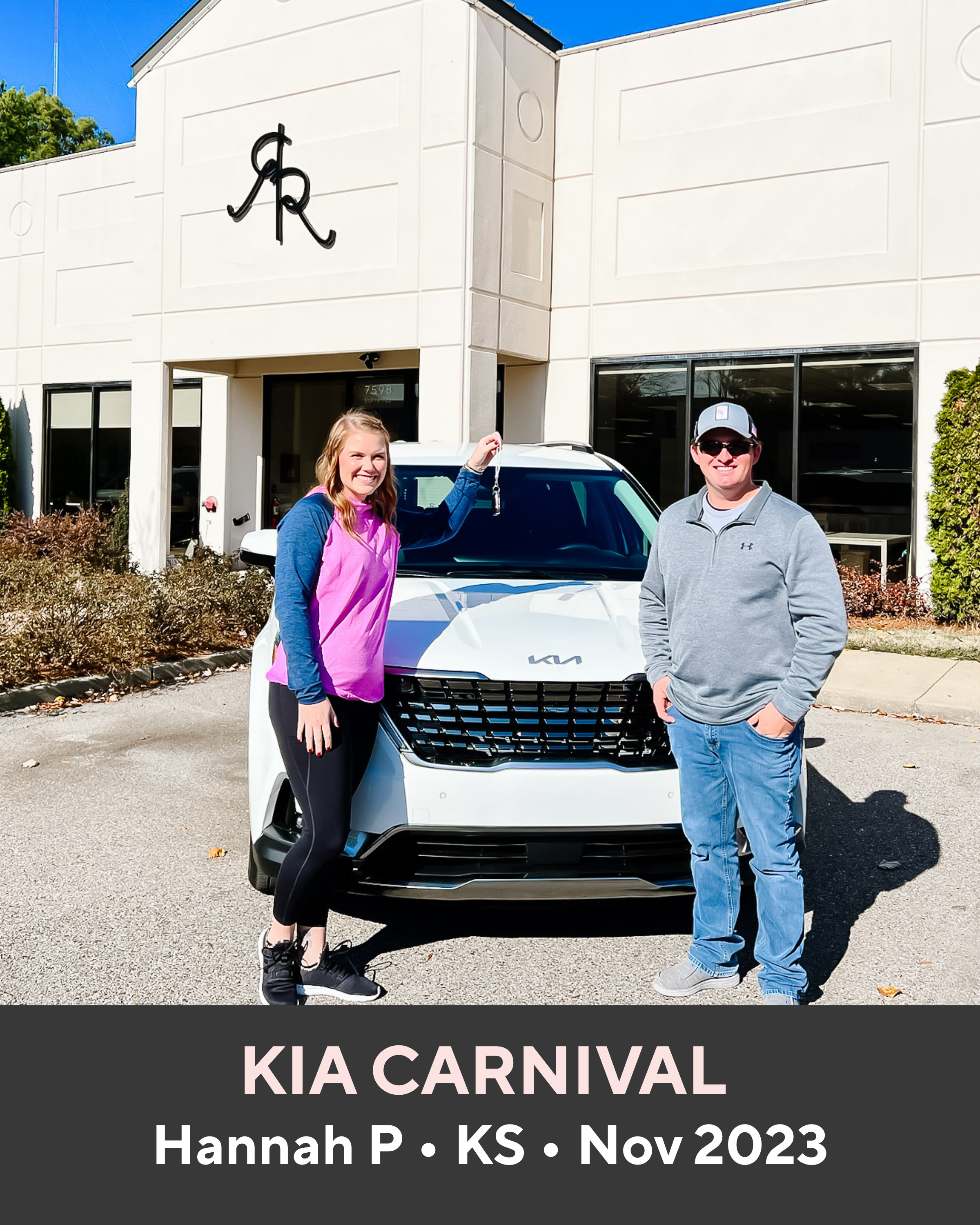 Two people standing next to a white Kia Carnival in front of a building with a logo.
