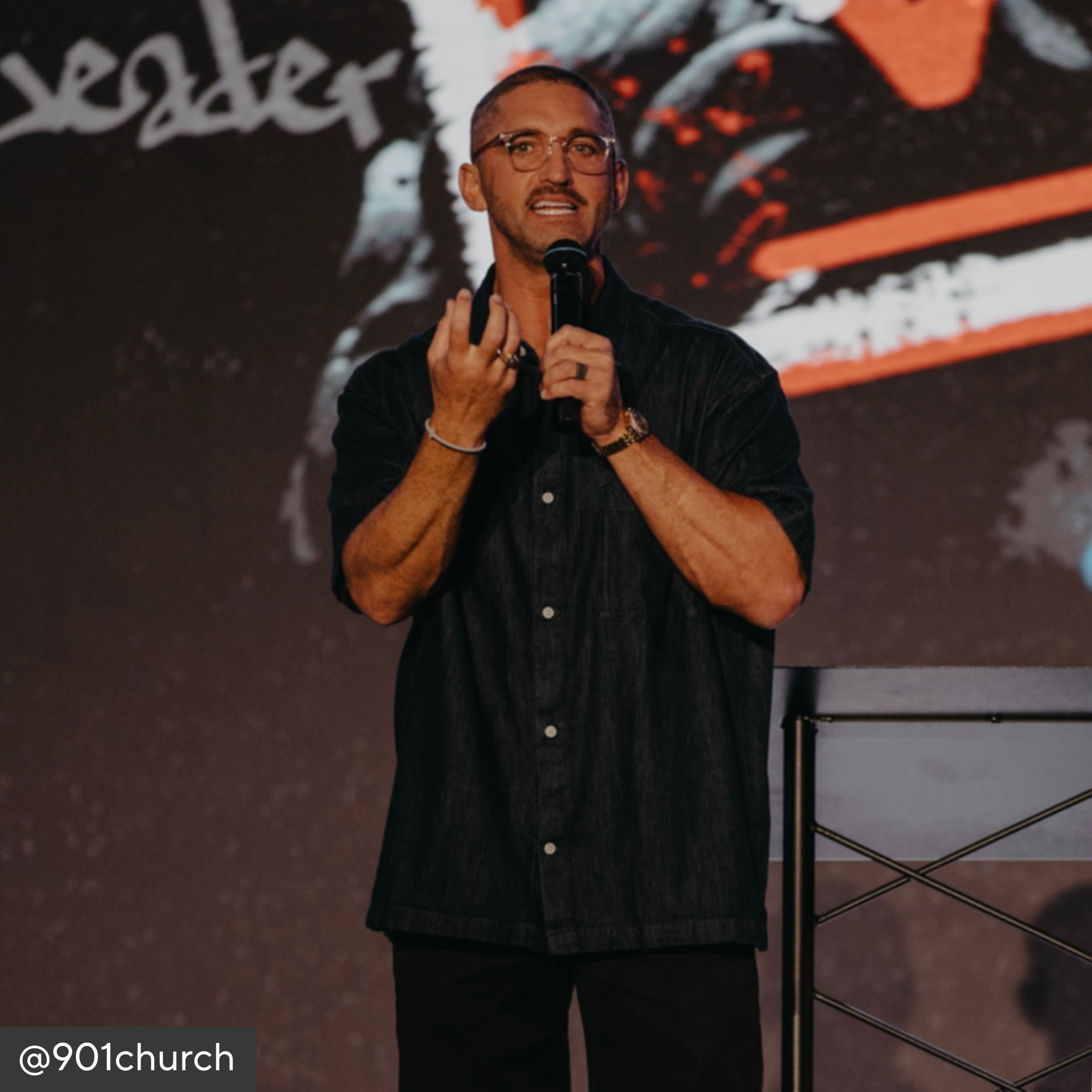 Man speaking into a microphone on a stage with a dark background