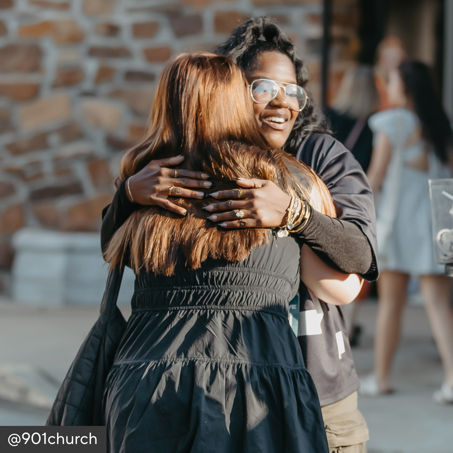 Two women hugging outdoors with a brick wall background