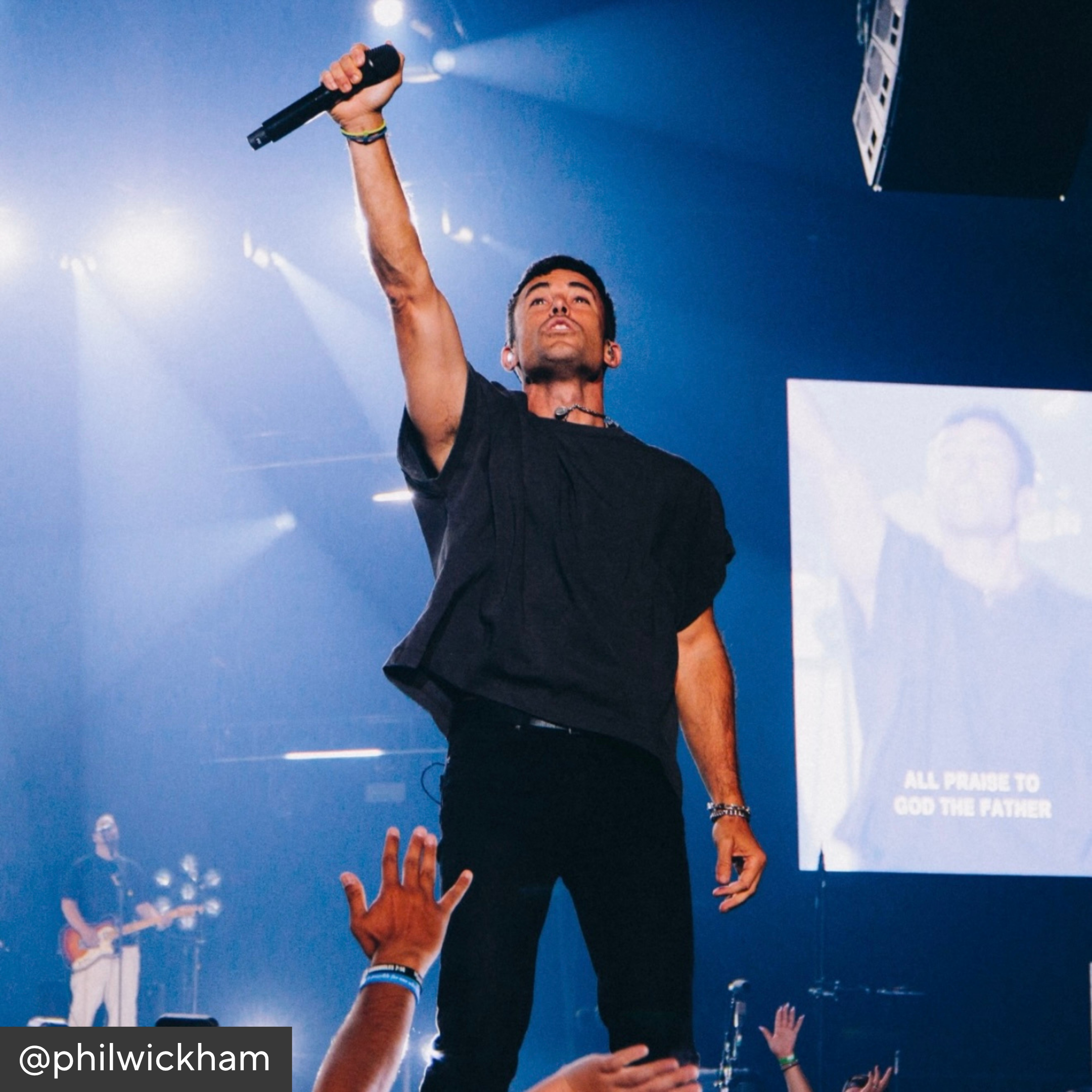 Phil Wickham on stage with microphone, audience hands raised, blue lighting