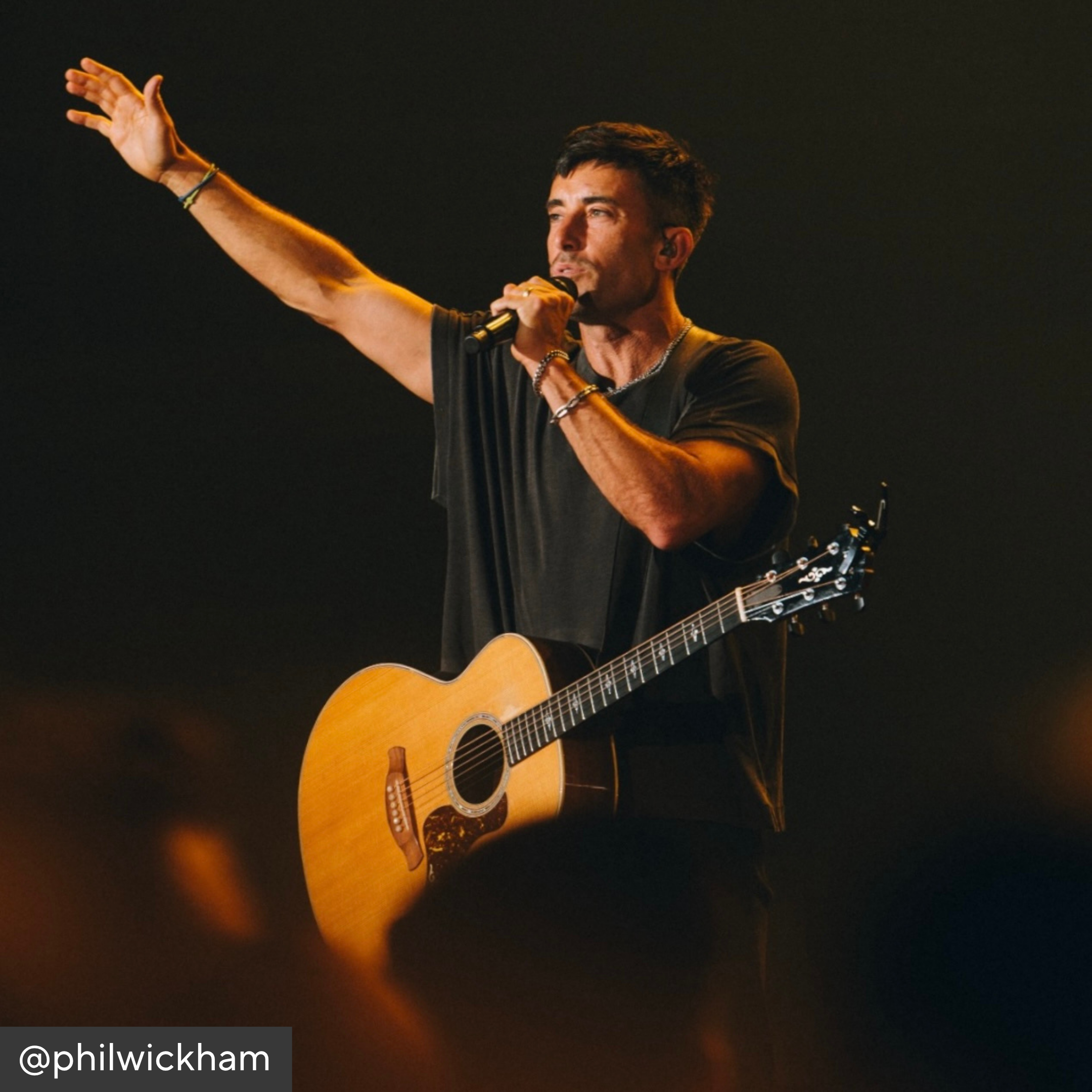Phil Wickham playing guitar and singing on stage with a dark background