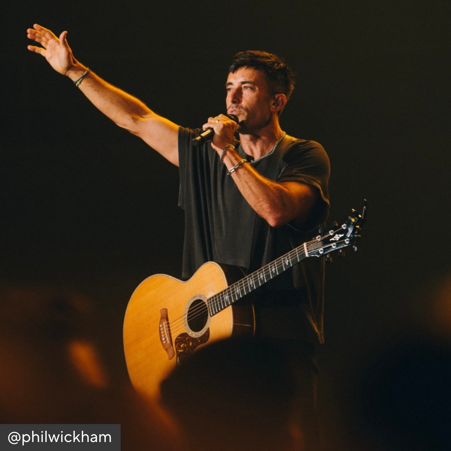 Phil Wickham playing guitar and singing on stage with a dark background