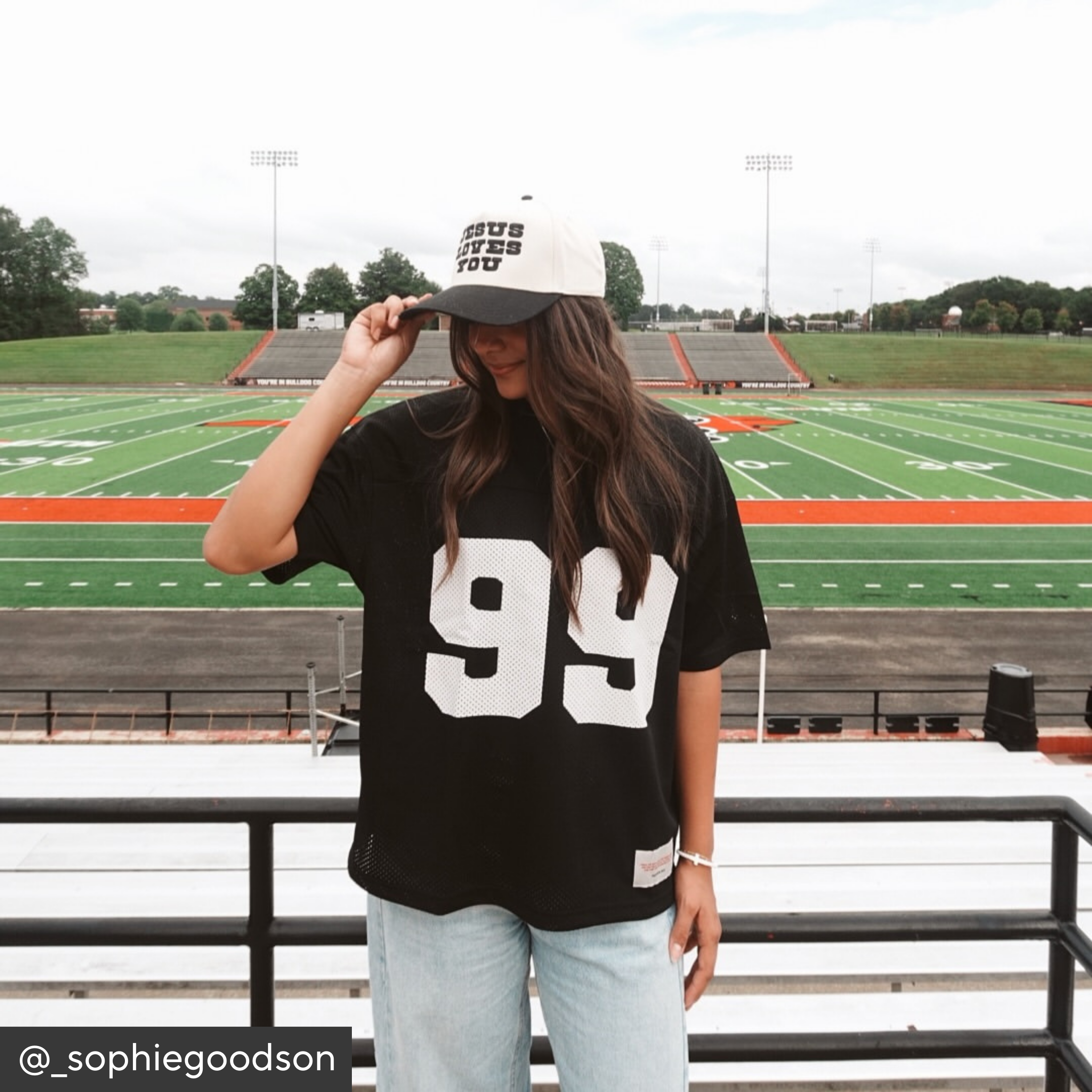 Person wearing a black t-shirt with number 99 and a cap on a football field.