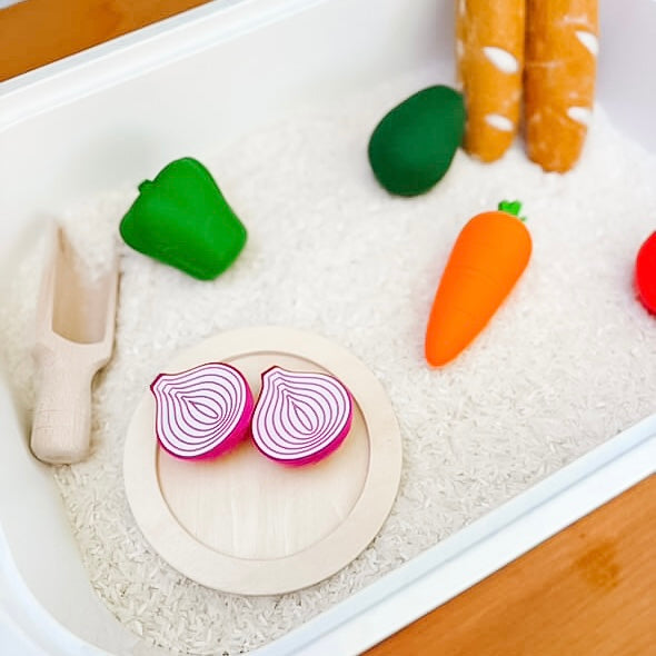Play food set with toy vegetables and utensils in a white sensory tray.