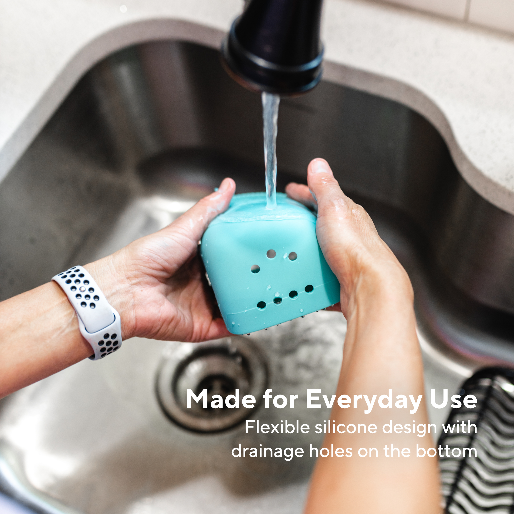 Person holding a blue silicone kitchen tool under running water in a sink with text about its flexibility and drainage holes.