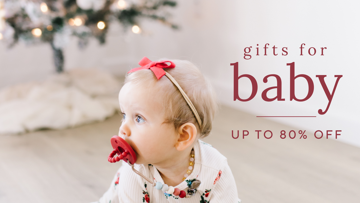 Baby with a pacifier sitting in front of a Christmas tree on a baby sale promotion banner