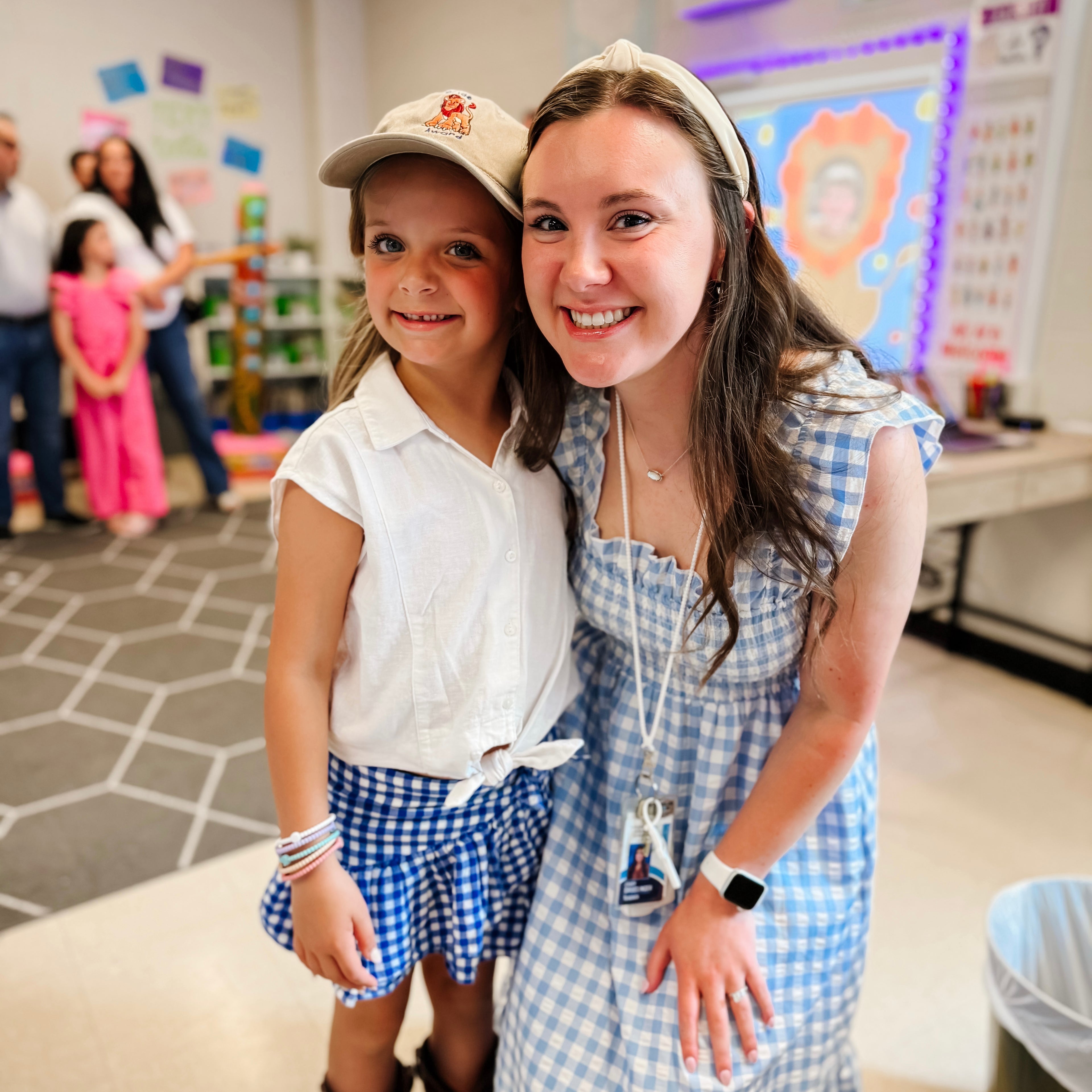 Two young girls posing together in a classroom setting with educational posters on the wall.