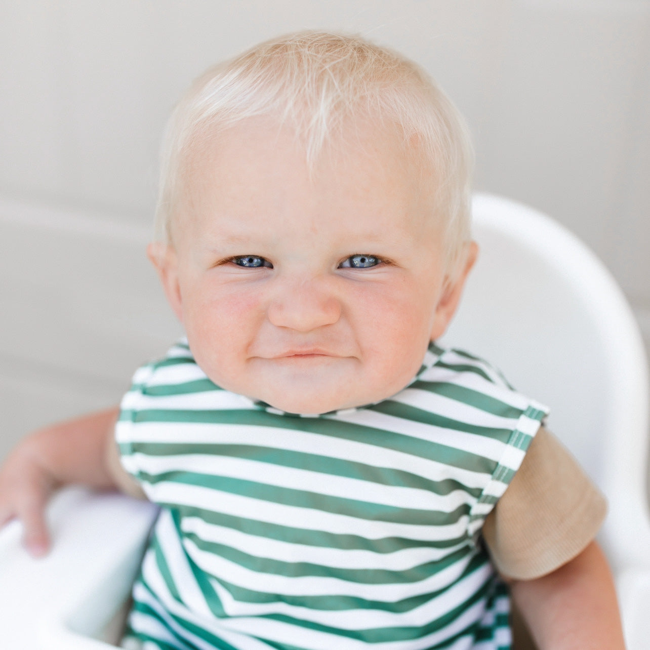 Baby sitting in a high chair wearing the Green Stripe Cutie Bapron.