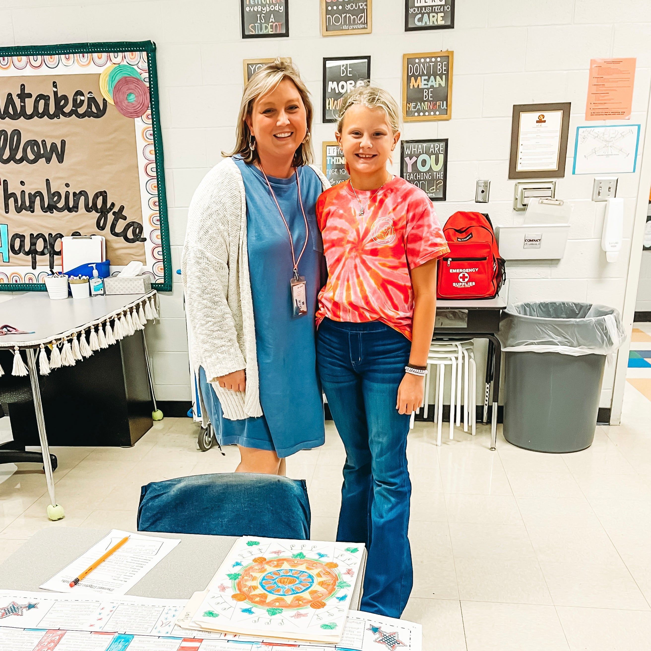 Teacher and student standing in a classroom with educational materials on the floor.