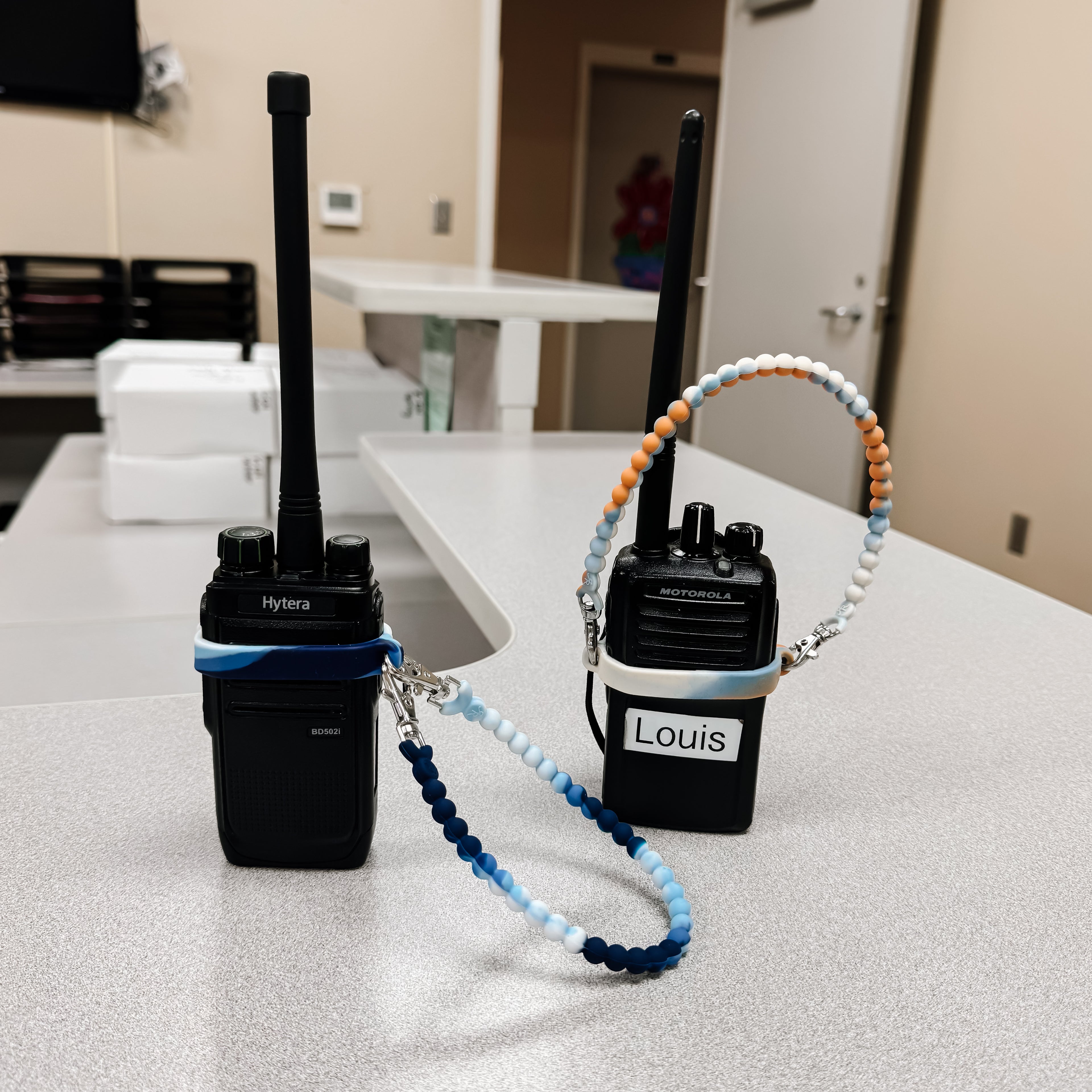 Two walkie-talkies with name tags on a table in an indoor setting