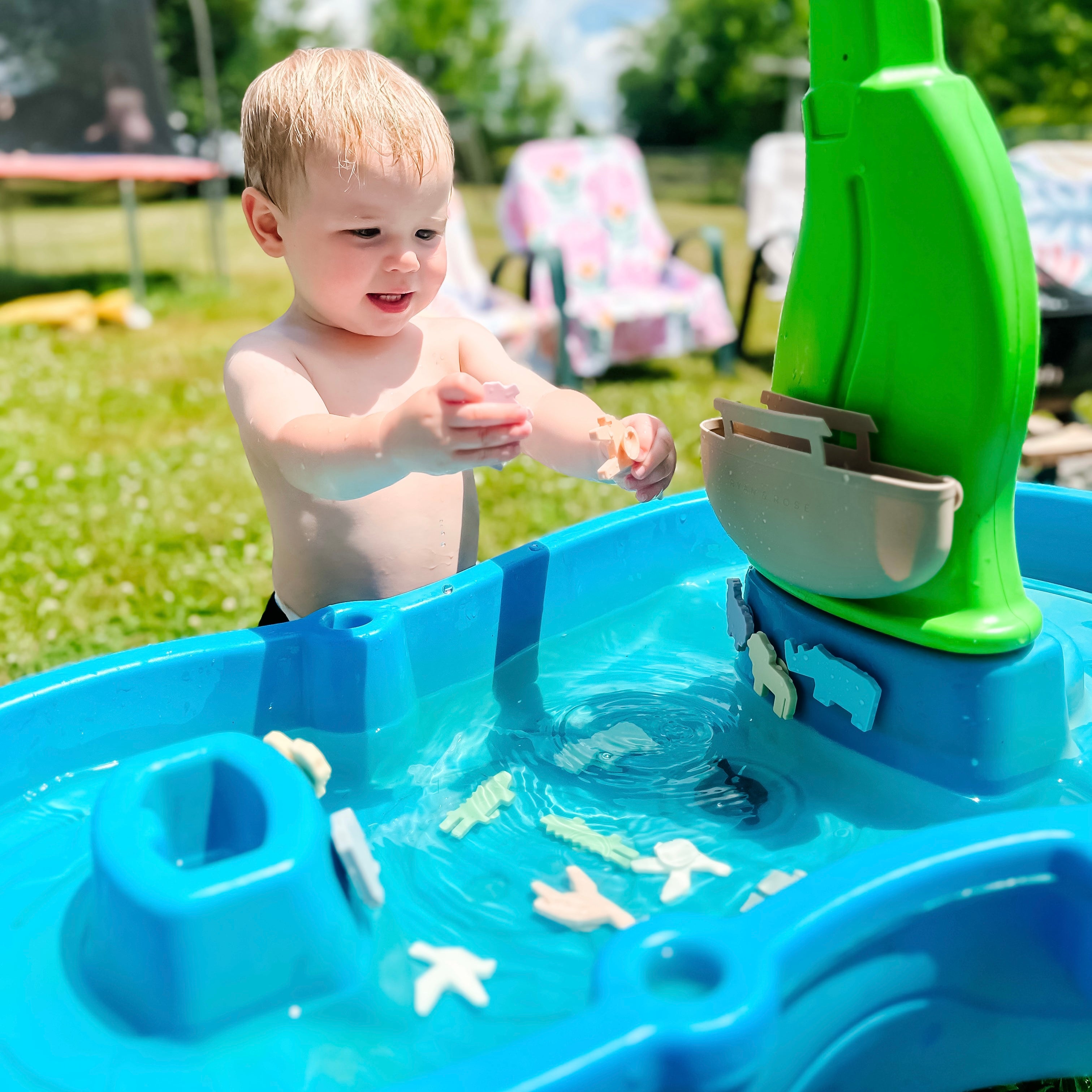 Child playing with a blue and green toy water table outdoors.