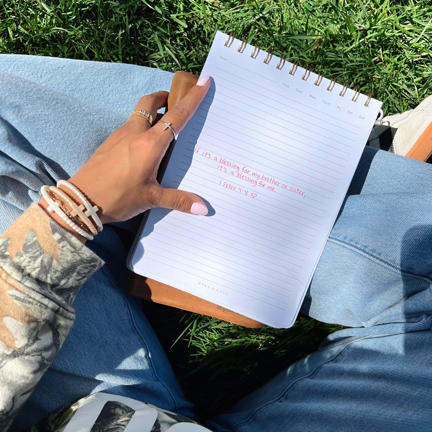 Person holding a spiral-bound notebook with text on grass