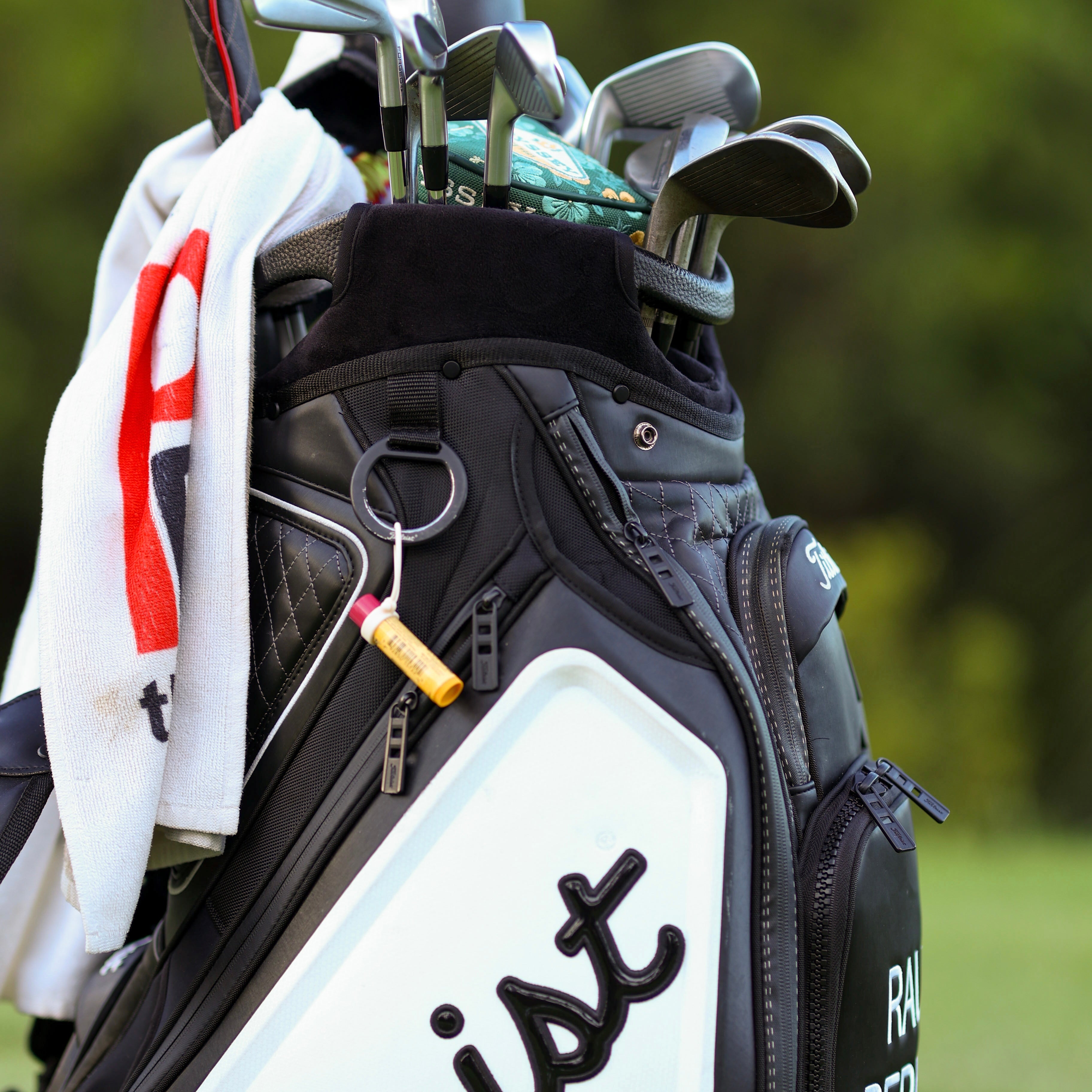 Golf bag with clubs and a towel on a blurred green background
