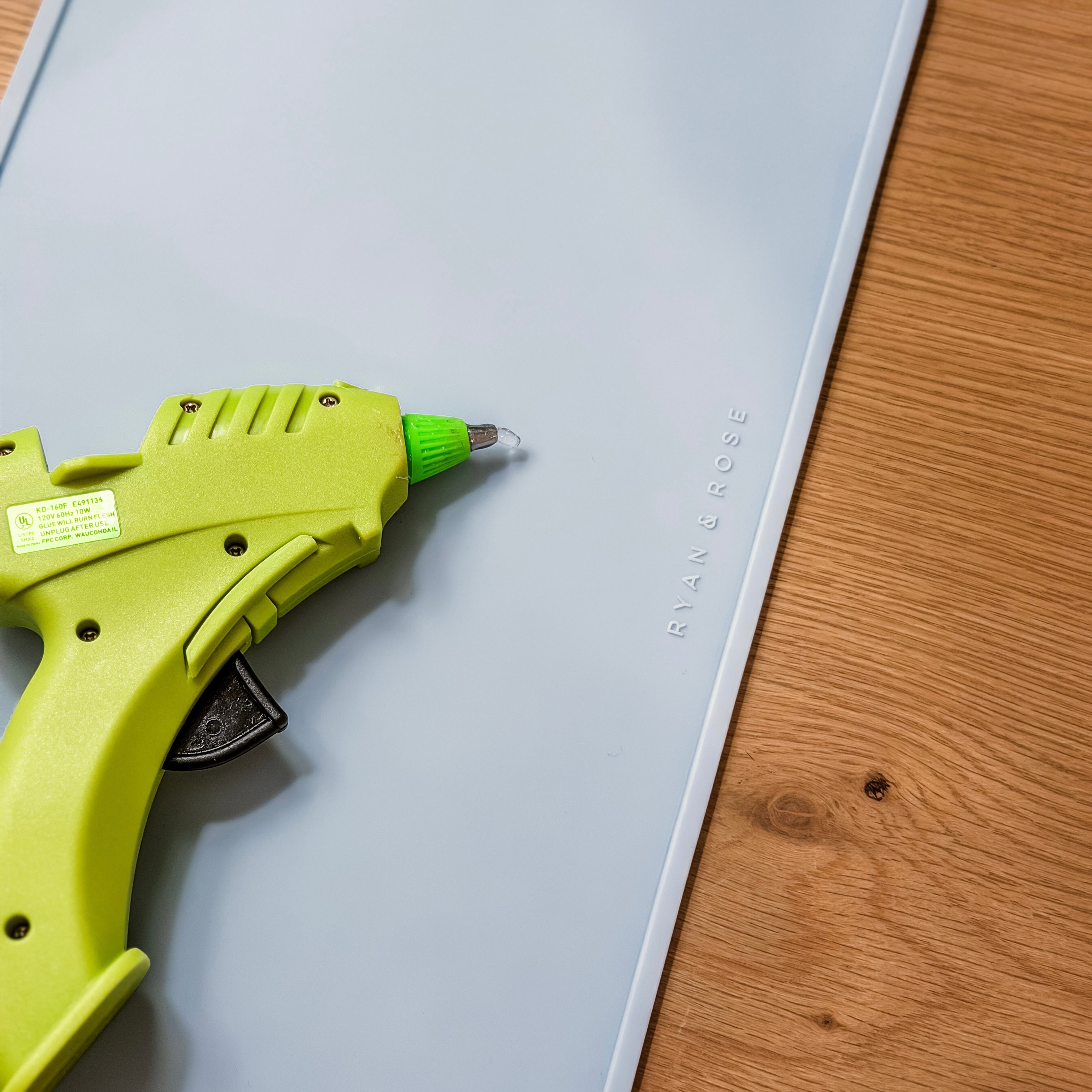 Green glue gun on a white surface with wooden edge