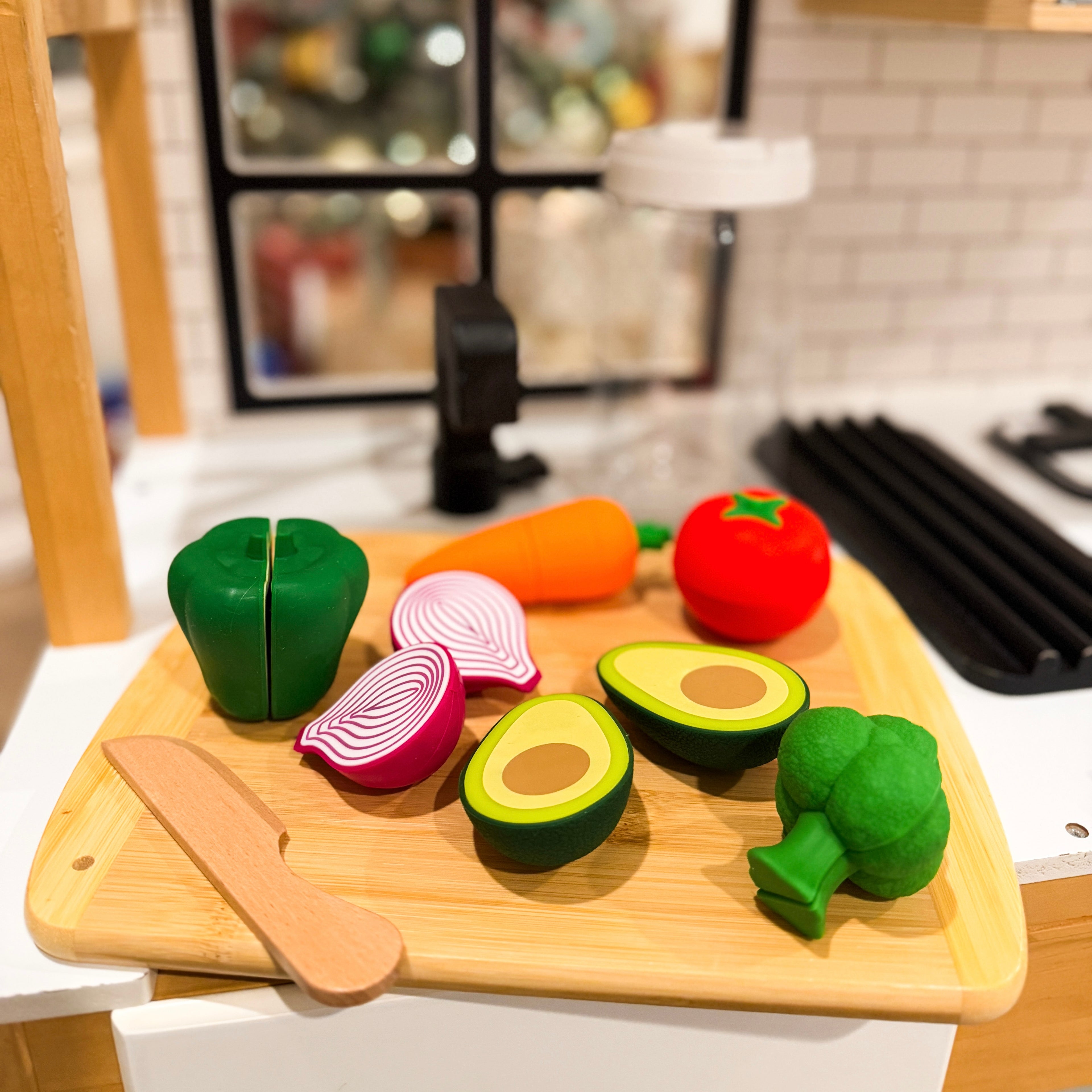 Set of toy vegetables and a knife on a wooden cutting board in a kitchen setting.