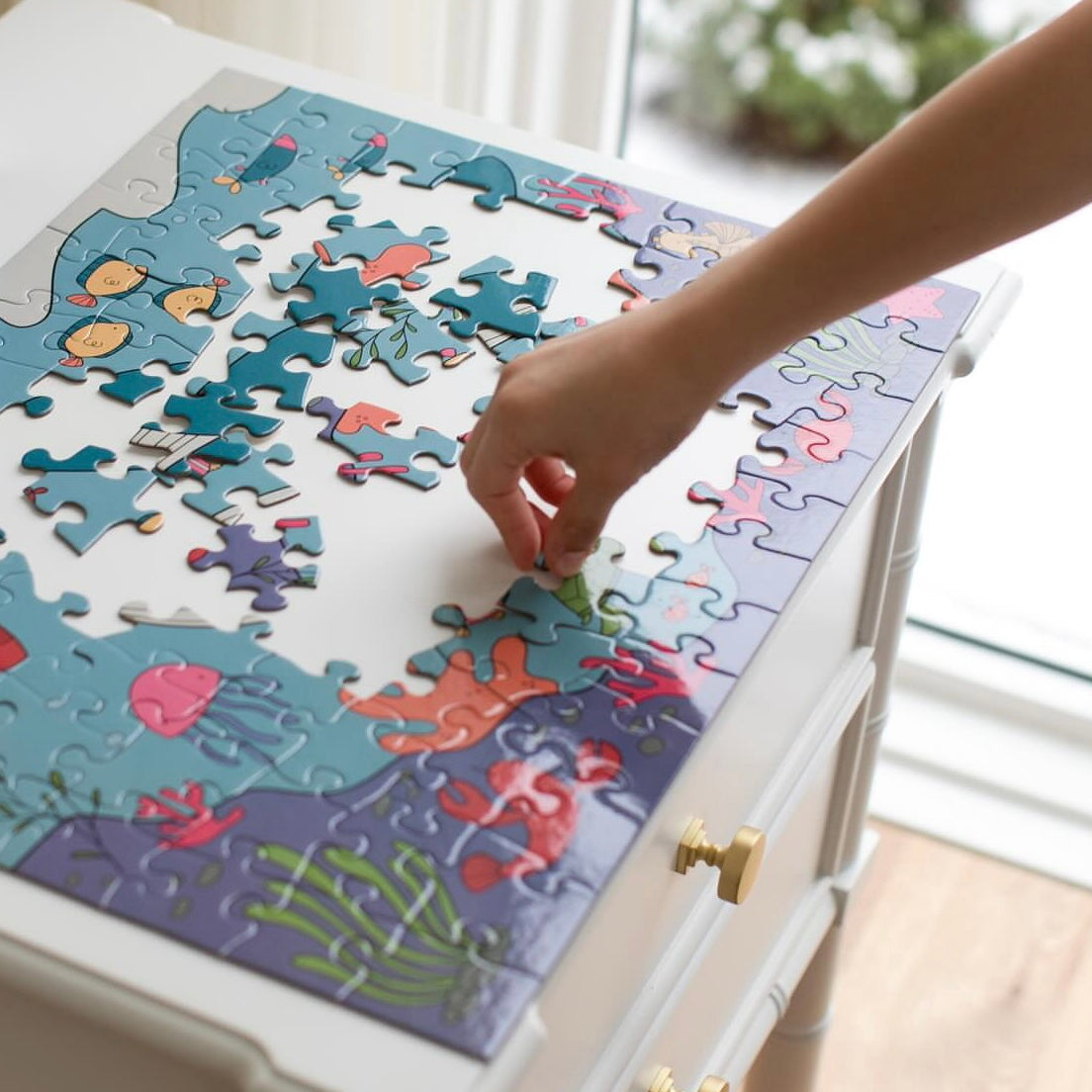 Person assembling a colorful puzzle on a white table.