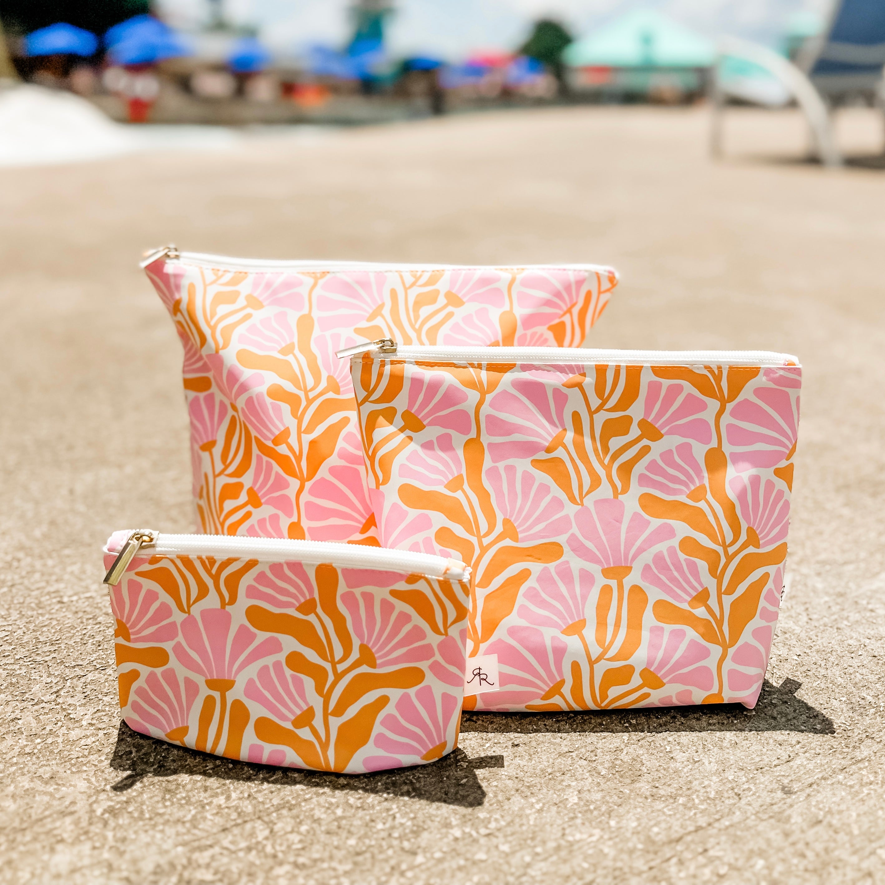 Three pink and orange patterned bags on a sandy surface with blurred background