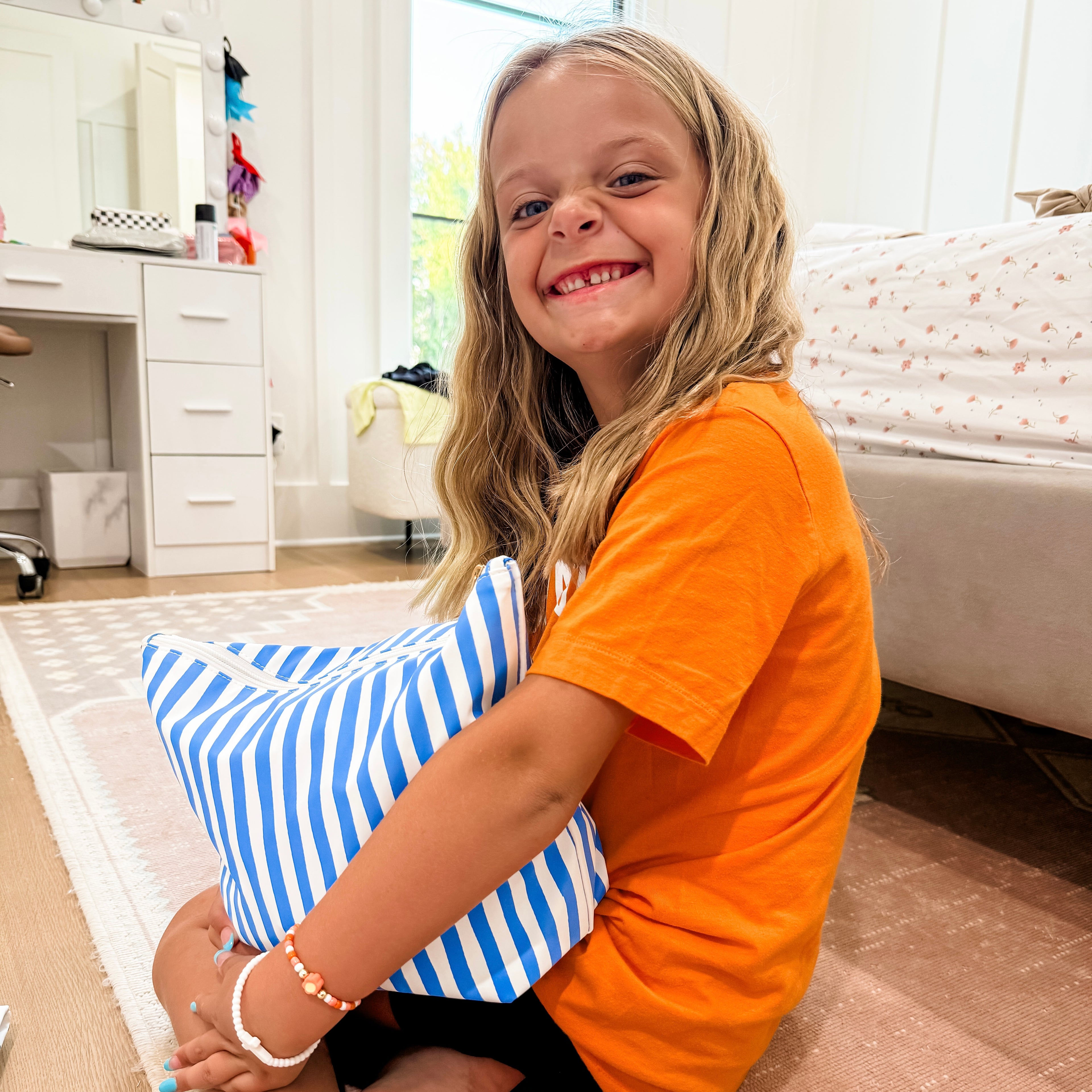 Child holding a blue and white striped pillow in a room with furniture and decor.