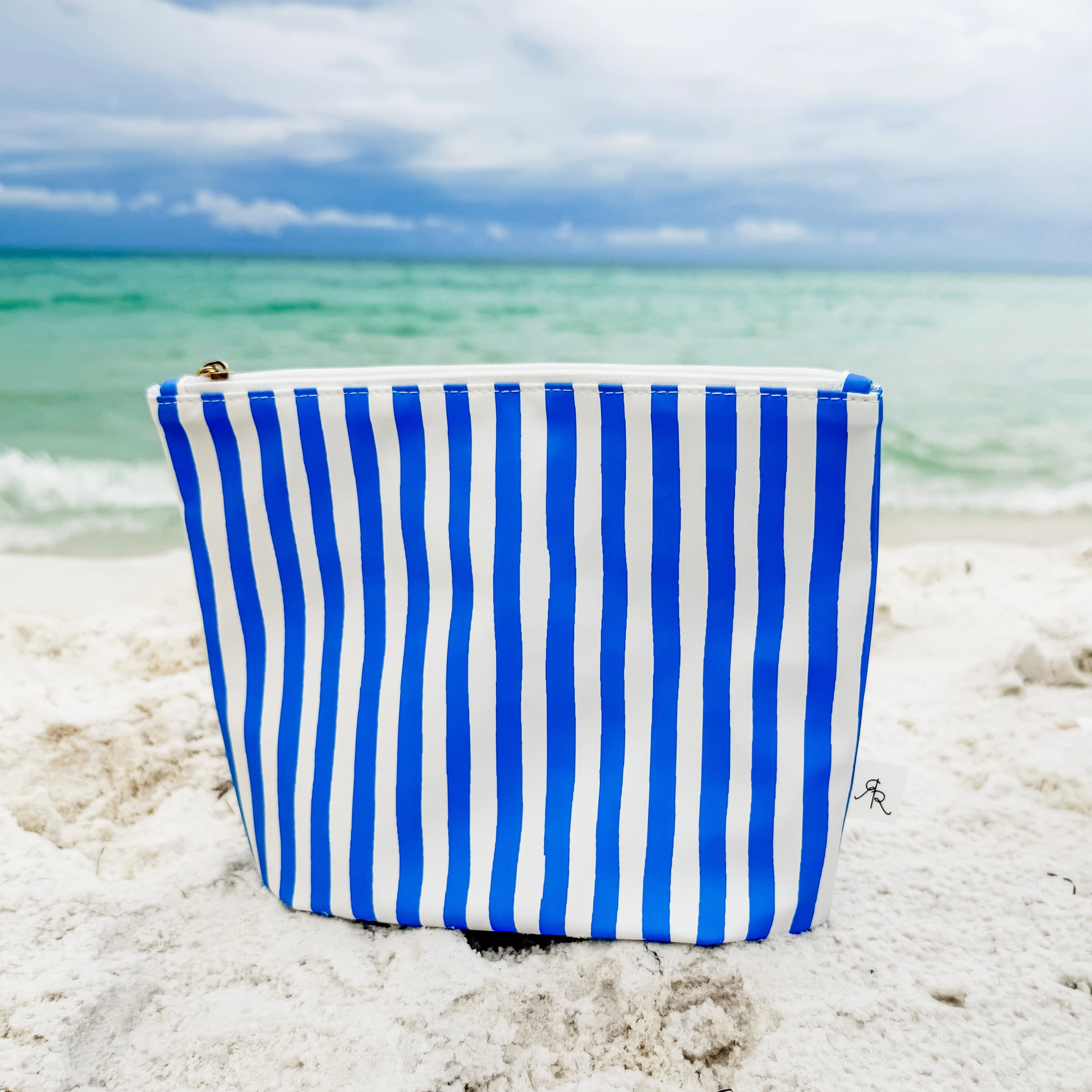 Blue and white striped bag on a sandy beach with ocean in the background