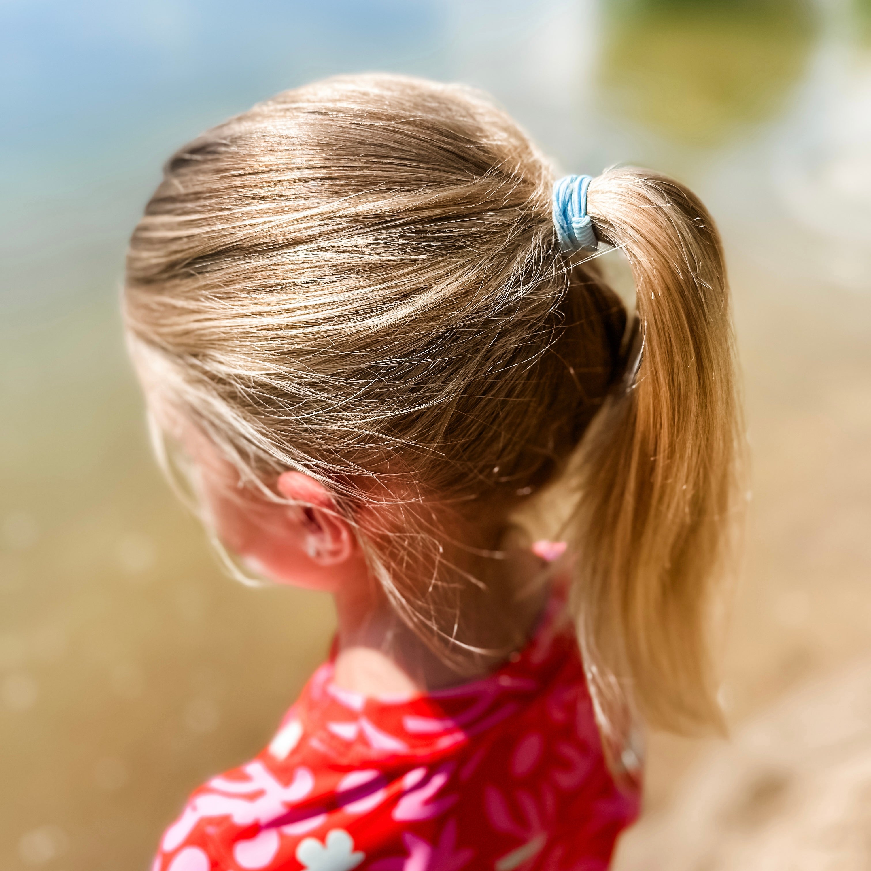 Back view of a child with blonde hair in a ponytail wearing a red polka dot shirt.