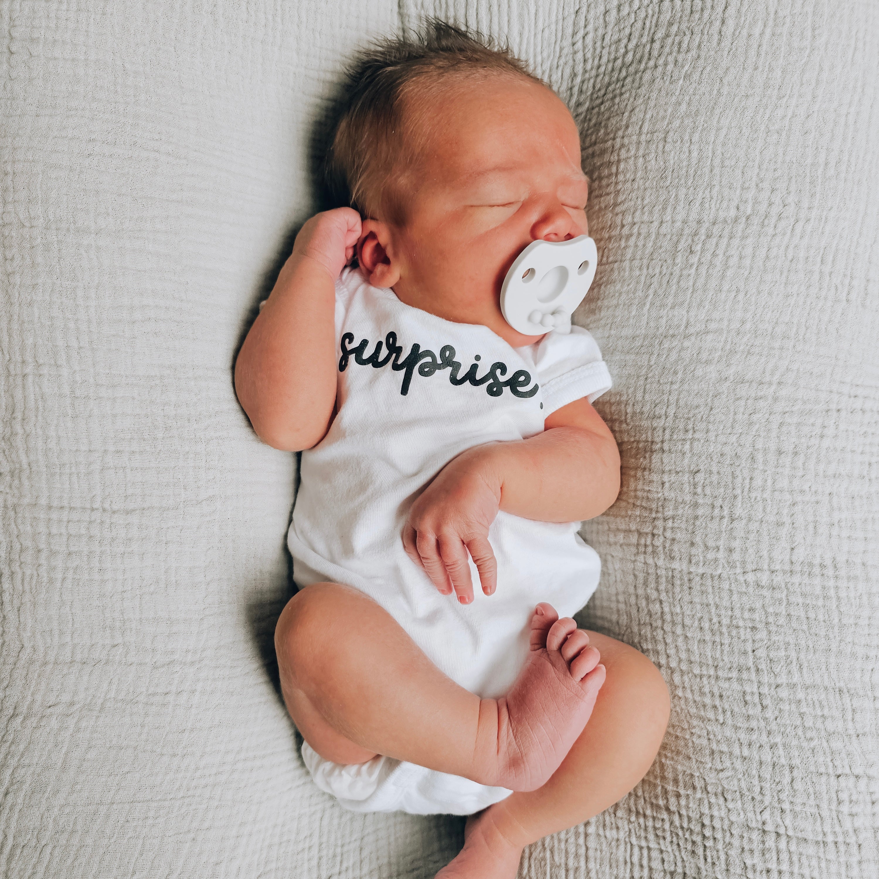 Newborn baby wearing a white onesie with &