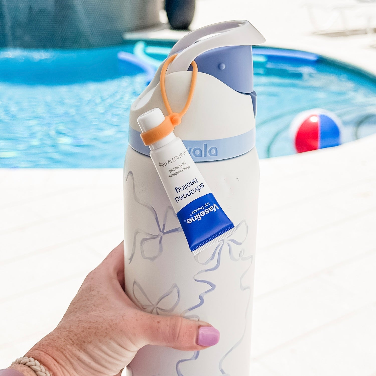 Hand holding a white water bottle with blue accents and a visible brand label, against a blurred pool background.