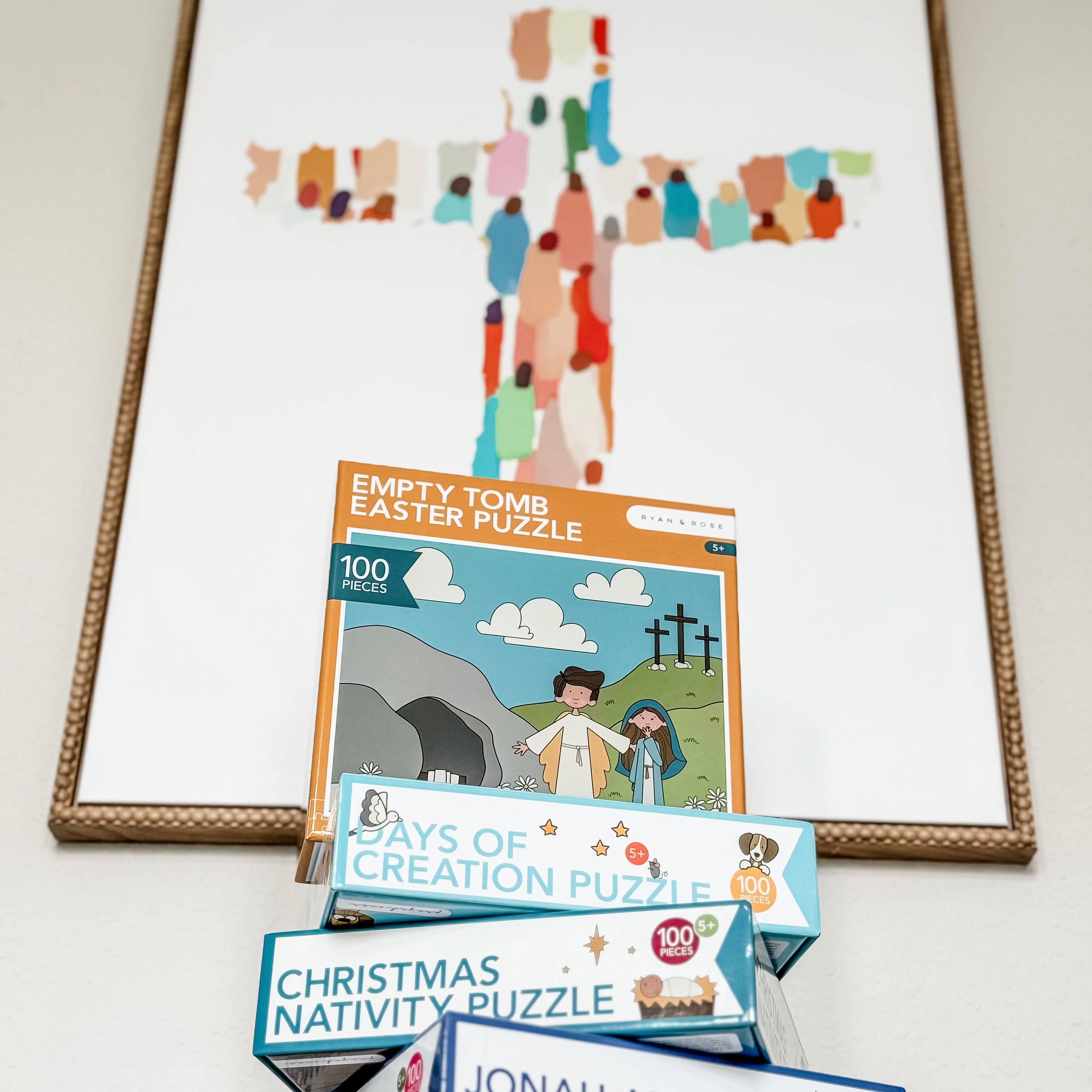 Set of religious-themed puzzles on a white surface with a framed cross in the background.