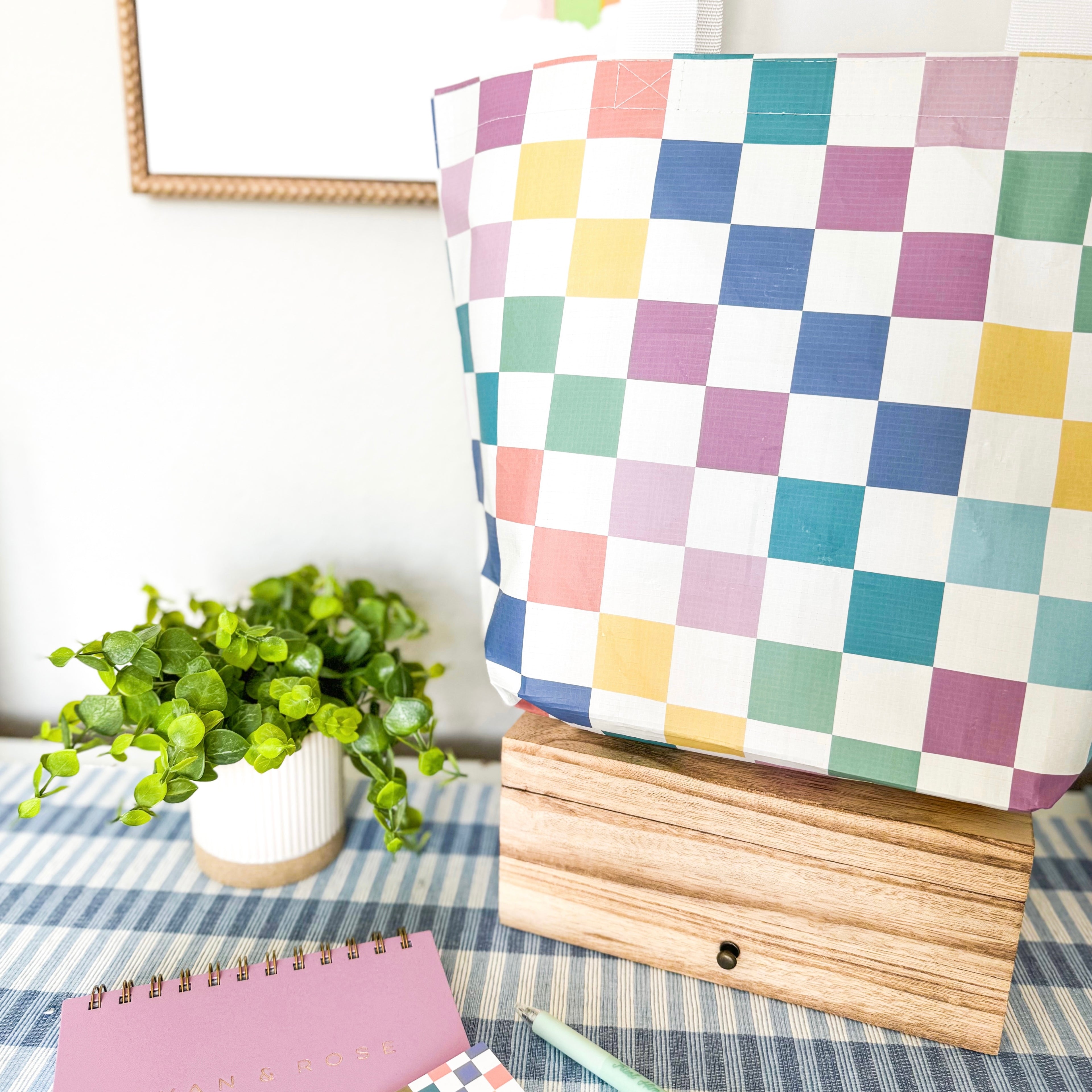 Checkered fabric on a wooden box with a plant and notebook in the background