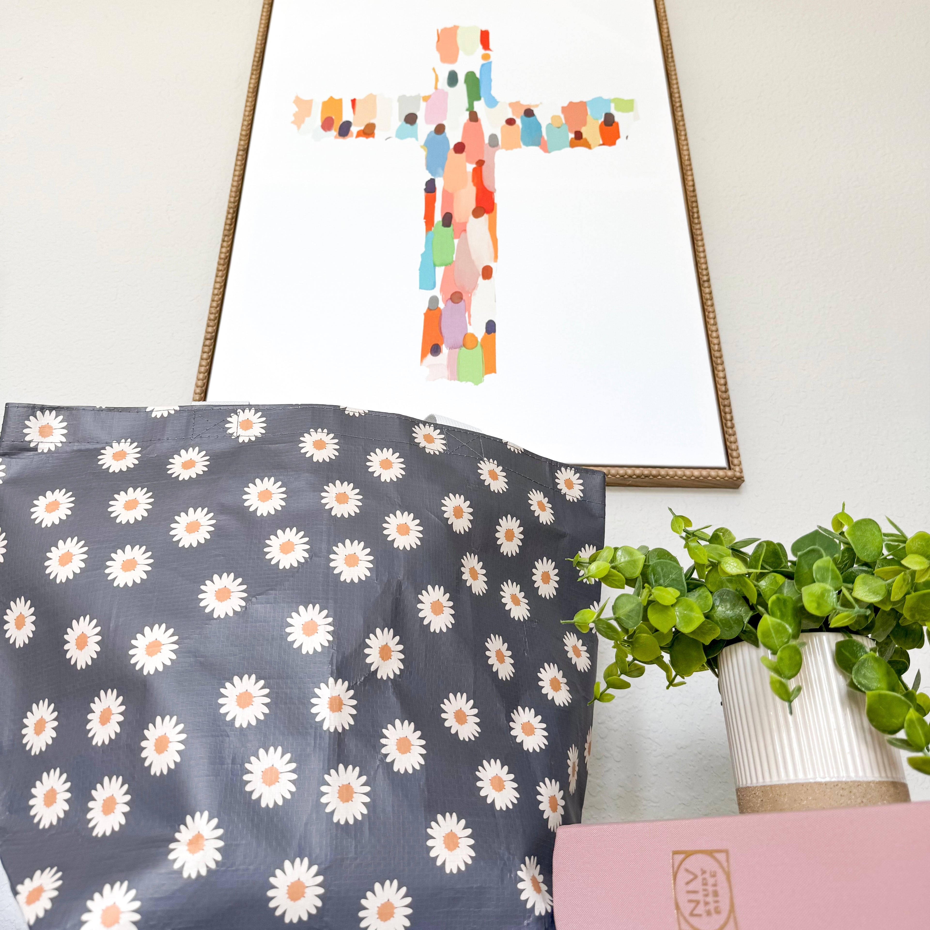 Decorative bag with daisy pattern, framed abstract art, and plant on a light background