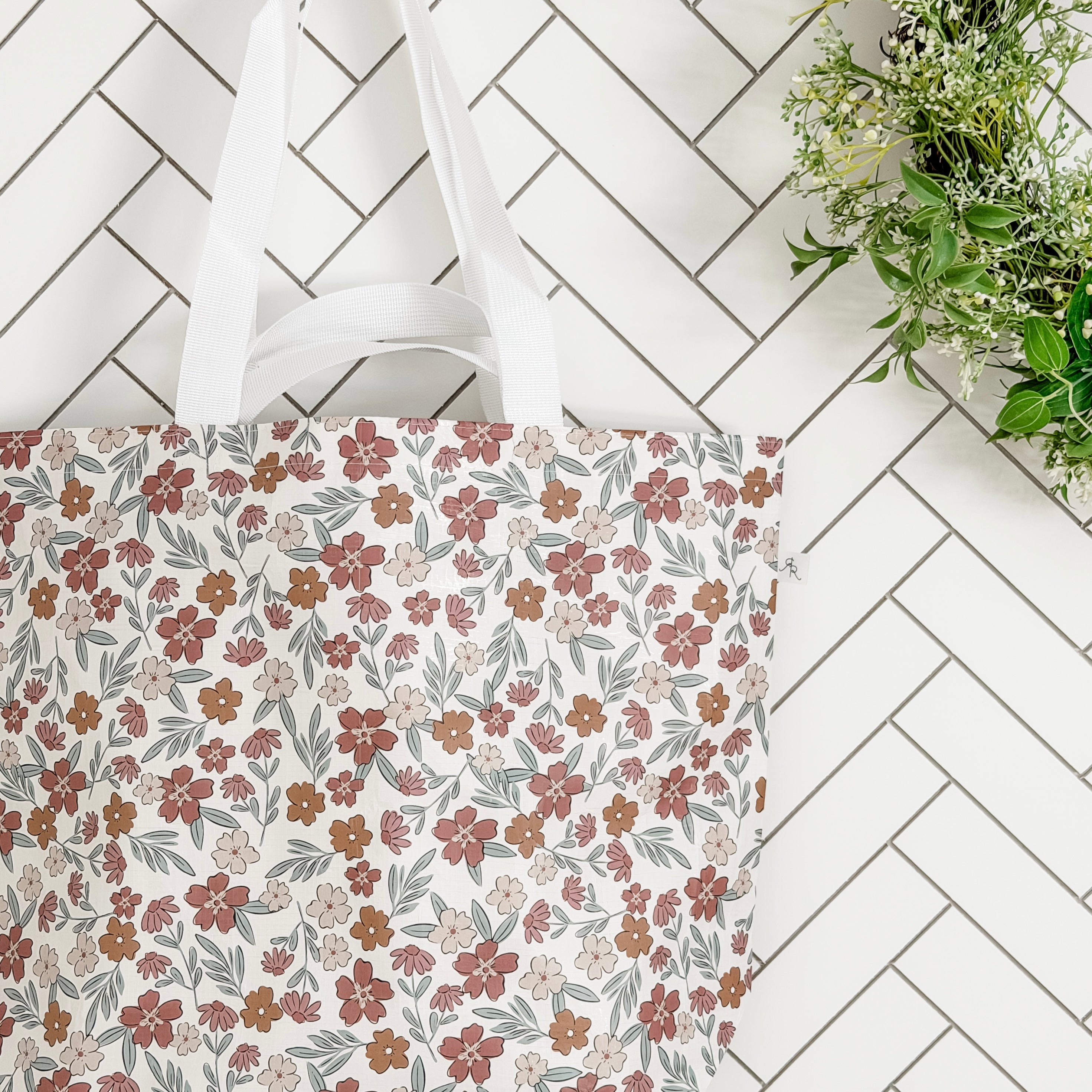 Floral-patterned tote bag on a white tiled floor with a plant in the corner