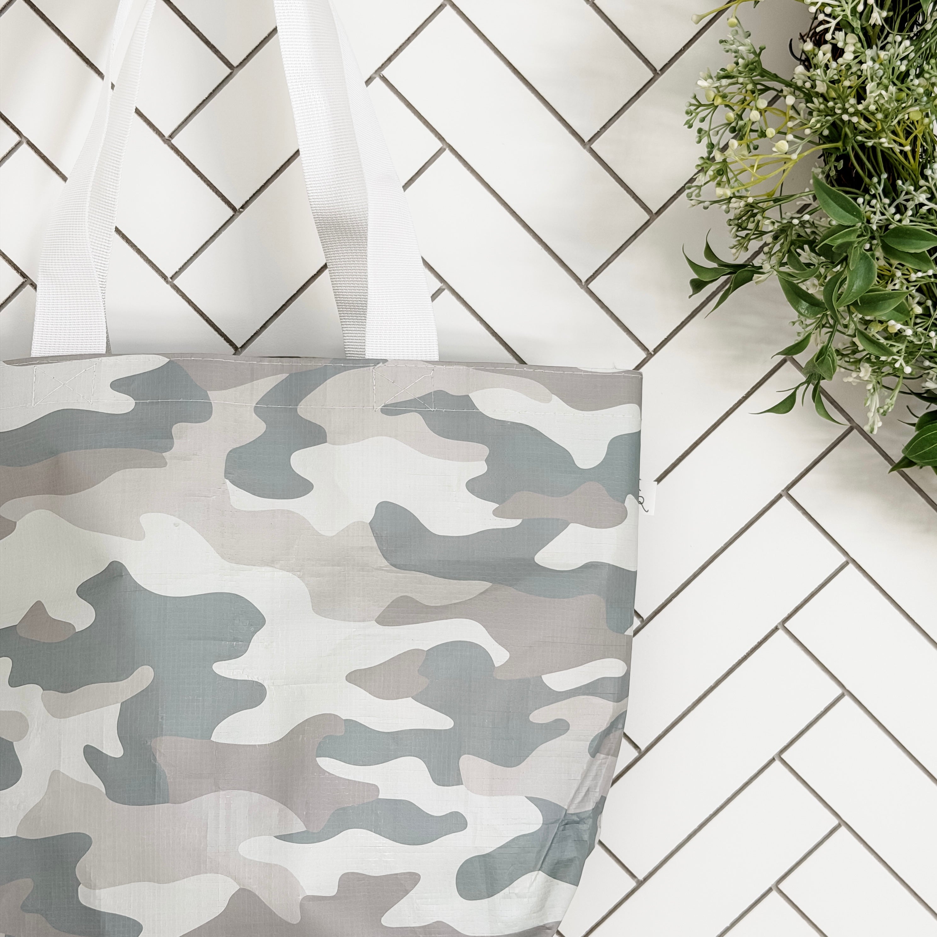 Camouflage-patterned bag on a tiled bathroom floor with a plant.
